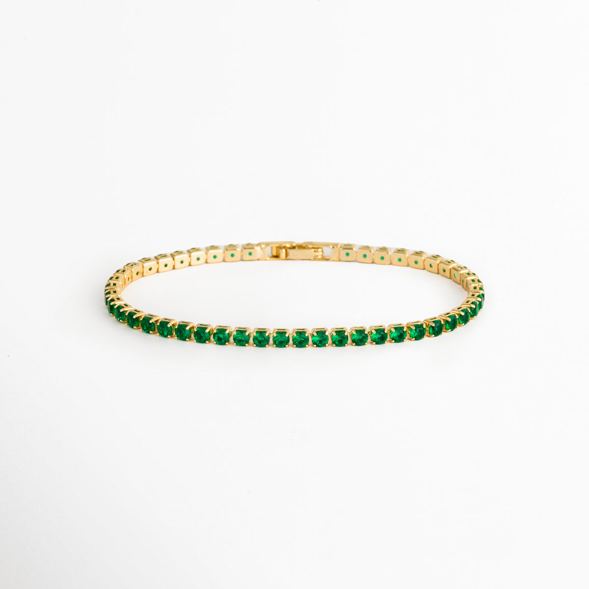 Tennis Bracelet Green Grace enchapada en oro 18K con hilera continua de circonias verde esmeralda de corte brillante, vista de frente sobre fondo blanco, Vista frontal de pulsera tennis delgada de 0.3 cm de ancho con gemas de circonia verde y engaste de garras doradas, Plano general de brazalete estilo tennis de cobre enchapado en oro 18K con pedrería verde brillante, Tennis Bracelet Green Grace mostrando la secuencia uniforme de circonias verdes de 18 cm