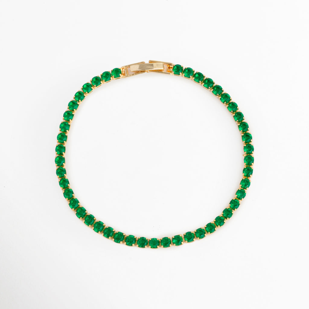 Vista superior en forma circular de la Tennis Bracelet Green Grace resaltando la simetría de sus circonias verde esmeralda, Toma aérea del brazalete tennis cerrado mostrando el contraste entre el baño de oro 18K y el tono verde profundo de las piedras, Plano cenital de pulsera elástica/articulada con hilera de circonias redondas verdes sobre fondo blanco, Muestra de la silueta perfecta de la pulsera de 18 cm de longitud con broche desplegable oculto.