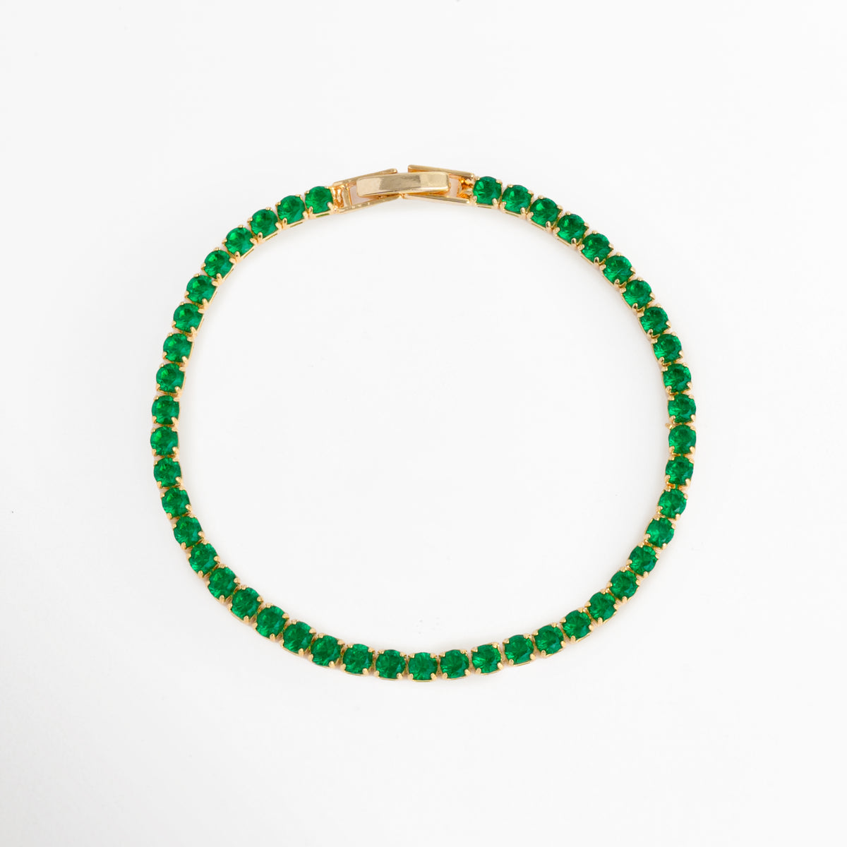 Vista superior en forma circular de la Tennis Bracelet Green Grace resaltando la simetría de sus circonias verde esmeralda, Toma aérea del brazalete tennis cerrado mostrando el contraste entre el baño de oro 18K y el tono verde profundo de las piedras, Plano cenital de pulsera elástica/articulada con hilera de circonias redondas verdes sobre fondo blanco, Muestra de la silueta perfecta de la pulsera de 18 cm de longitud con broche desplegable oculto.