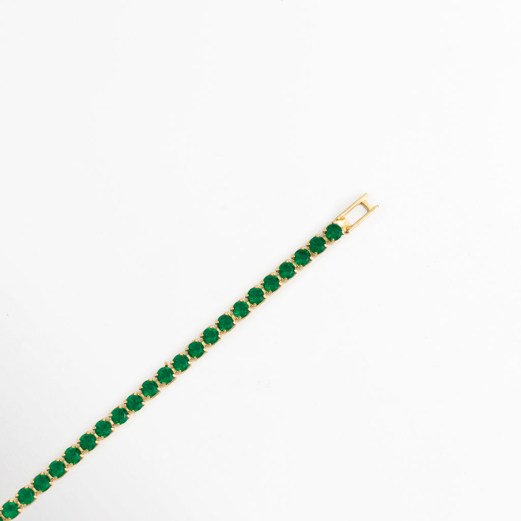 Acercamiento a la línea recta de la Tennis Bracelet Green Grace y al broche de caja o desplegable enchapado en oro 18K, Vista en diagonal del cierre metálico de seguridad tipo joyería y los eslabones articulados de circonias verdes, Detalle de la confección de 0.3 cm de ancho con engaste individual de micro-garras doradas, Muestra de la terminación metálica pulida y el sistema de ajuste seguro del brazalete verde.