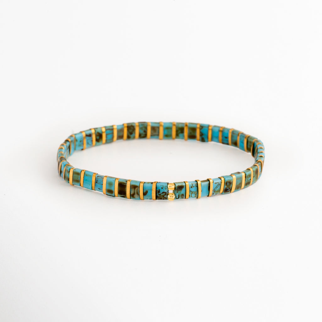Pulsera Rectángulos Aquamarina elaborada con cuentas Tila en tonos turquesa y dorado sobre fondo blanco, Vista frontal de la Pulsera Rectángulos Aquamarina con diseño elástico de cuentas rectangulares, Pulsera Rectángulos Aquamarina con cuentas Tila turquesa y doradas de estilo minimalista, Pulsera elástica Rectángulos Aquamarina con cuentas rectangulares en colores turquesa y dorado, Pulsera Rectángulos Aquamarina con diseño moderno de cuentas Tila sobre fondo blanco.