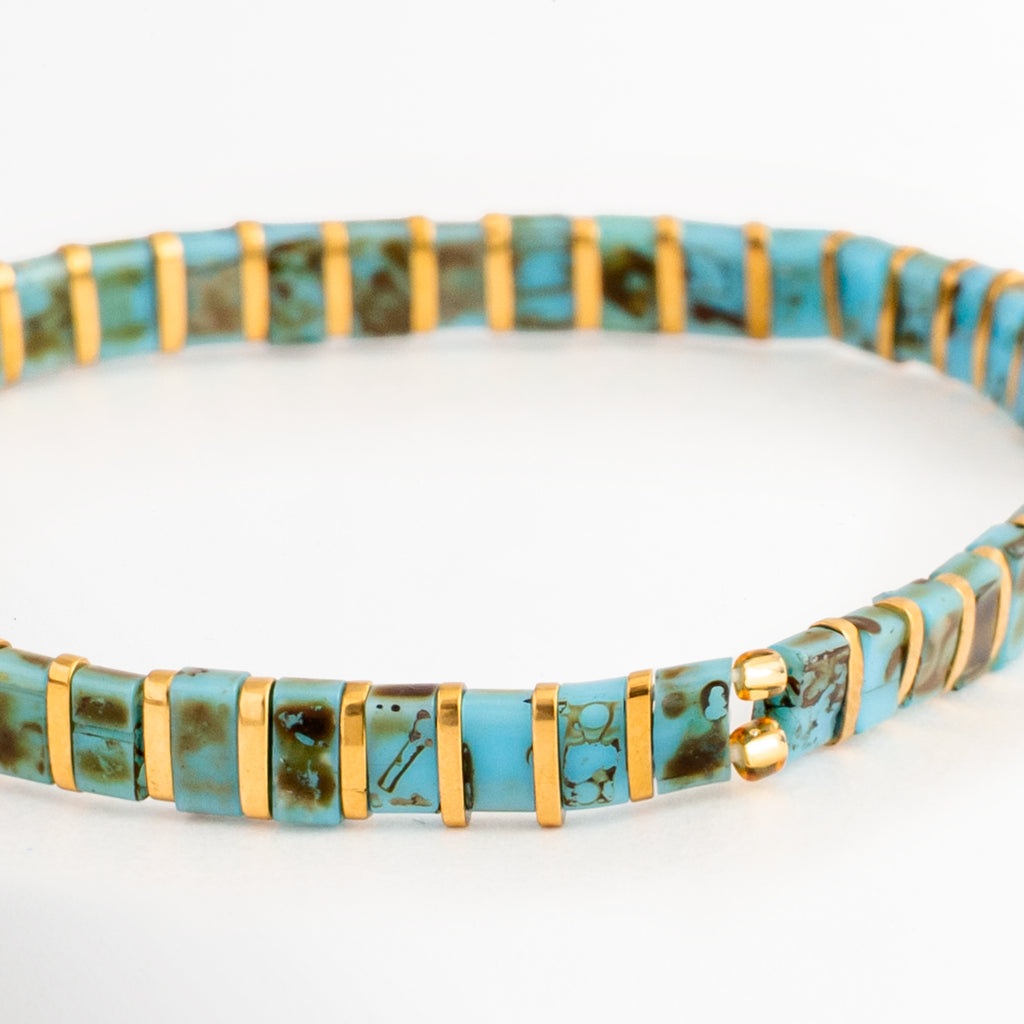 Acercamiento de la Pulsera Rectángulos Aquamarina mostrando las cuentas Tila en tonos turquesa y dorado, Detalle de las cuentas rectangulares de la Pulsera Rectángulos Aquamarina con acabado brillante, Vista cercana de la Pulsera Rectángulos Aquamarina resaltando el patrón de colores turquesa y dorado, Detalle de la Pulsera Rectángulos Aquamarina elaborada con cuentas Tila de estilo moderno, Acercamiento de la Pulsera Rectángulos Aquamarina mostrando la textura y combinación de colores de las cuentas.