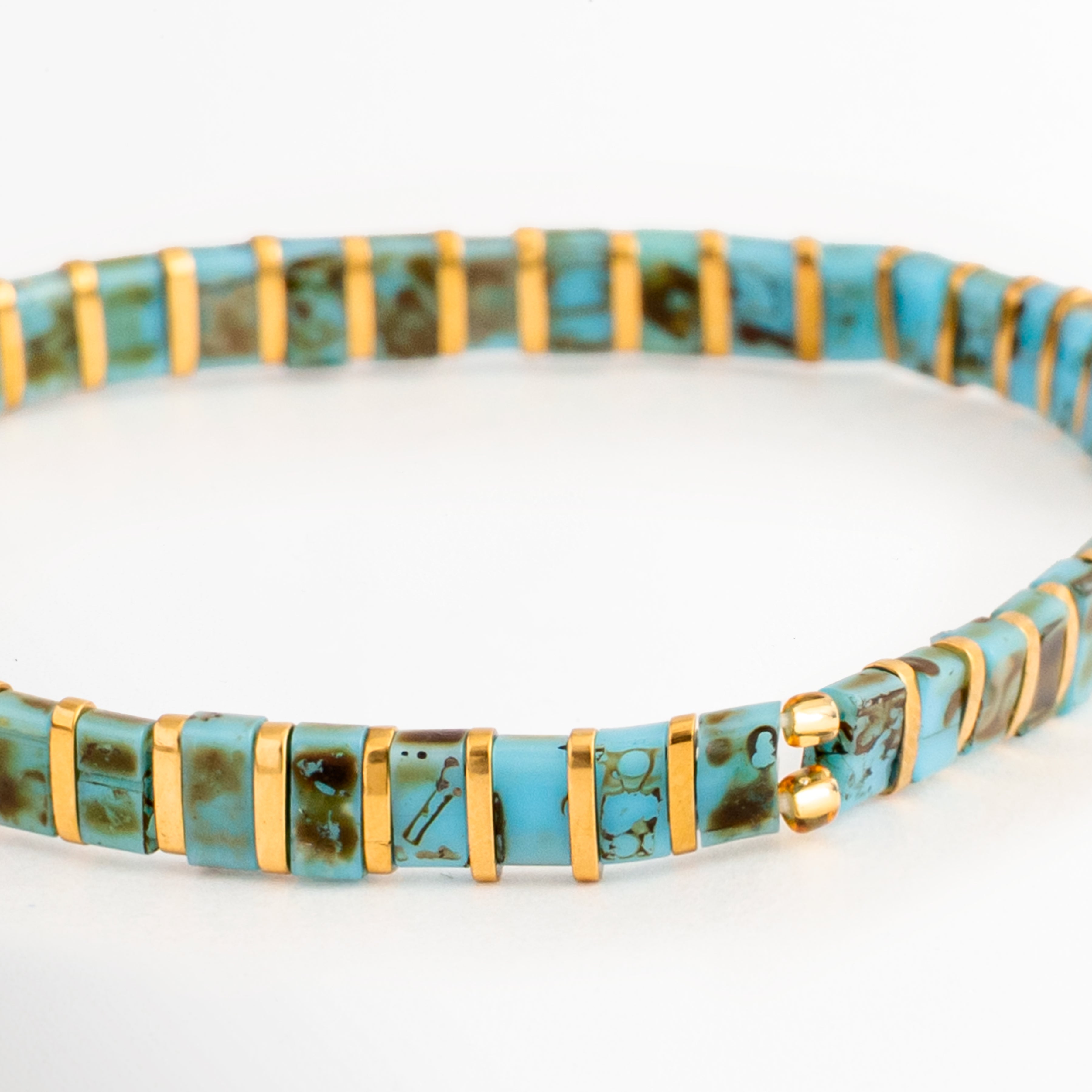 Acercamiento de la Pulsera Rectángulos Aquamarina mostrando las cuentas Tila en tonos turquesa y dorado, Detalle de las cuentas rectangulares de la Pulsera Rectángulos Aquamarina con acabado brillante, Vista cercana de la Pulsera Rectángulos Aquamarina resaltando el patrón de colores turquesa y dorado, Detalle de la Pulsera Rectángulos Aquamarina elaborada con cuentas Tila de estilo moderno, Acercamiento de la Pulsera Rectángulos Aquamarina mostrando la textura y combinación de colores de las cuentas.
