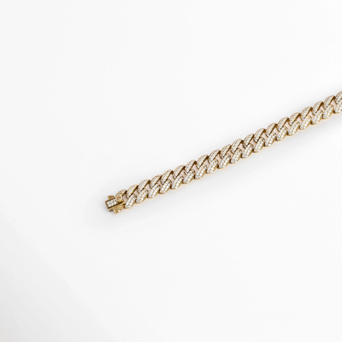 Vista en diagonal de la Pulsera Golden Margot extendida en línea recta resaltando el brillo cálido de su pavé de diamantes sintéticos, Acercamiento en perspectiva a la tira continua de eslabones cubanos aplanados de 0.9 cm sobre superficie neutra, Toma angular que enfatiza los destellos de luz sobre el acabado enchapado en oro 18K, Muestra del perfil ergonómico y el trabajo de engaste en la pulsera de plata ley 925.  