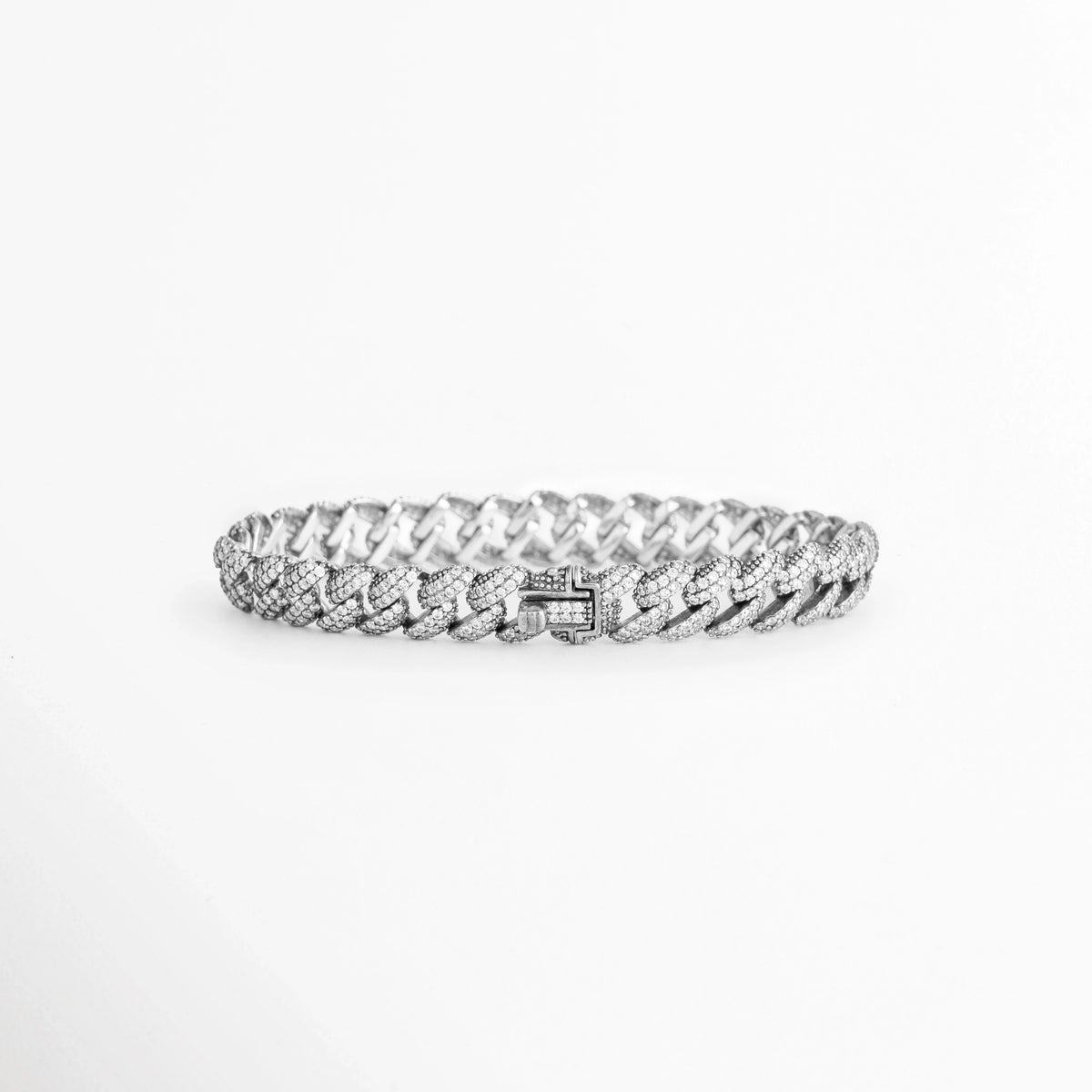 Vista en perspectiva de la Pulsera Silver Margot mostrando el broche de caja seguro integrado con pedrería en los eslabones cubanos, Acercamiento a la cara posterior del cierre plegable de la pulsera plateada enchapada en oro blanco 18K, Toma en ángulo que resalta la solidez y el pulido espejo de la plata ley 925 en el broche de la caden, Muestra del mecanismo de sujeción tipo reloj para un ajuste firme en la pulsera de 20 cm de longitud.