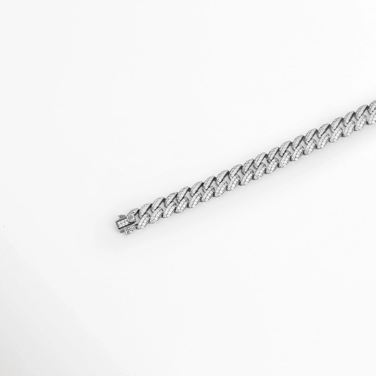 Vista en diagonal de la Pulsera Silver Margot extendida en línea recta resaltando el brillo helado de su pavé de diamantes sintéticos, Acercamiento en perspectiva a la tira continua de eslabones cubanos aplanados de 0.9 cm sobre superficie neutra, Toma angular que enfatiza los destellos de luz sobre el acabado enchapado en oro blanco 18K,  Muestra del perfil ergonómico y el trabajo de engaste en la pulsera de plata ley 925. 