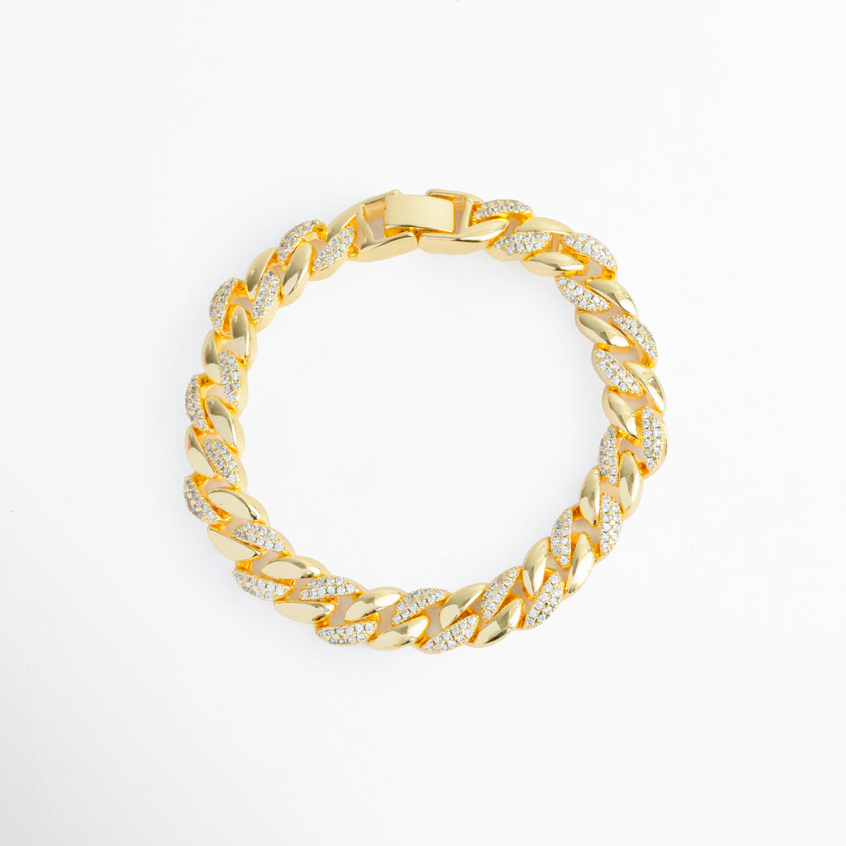 Pulsera Brock de eslabones estilo barbada cubana enchapada en oro 18K con incrustaciones de circonias tipo CZ en media cara, vista superior sobre fondo blanco, Vista de frente de gargantilla o pulsera cubana dorada de 0.6 cm de ancho con pavé de circonias transparentes sobre eslabones entrelazados, Plano general de cadena tipo cubana de cobre enchapada en oro 18K con destellos de pedrería fina sobre fondo neutro, Pulsera Brock destacando la simetría de sus eslabones