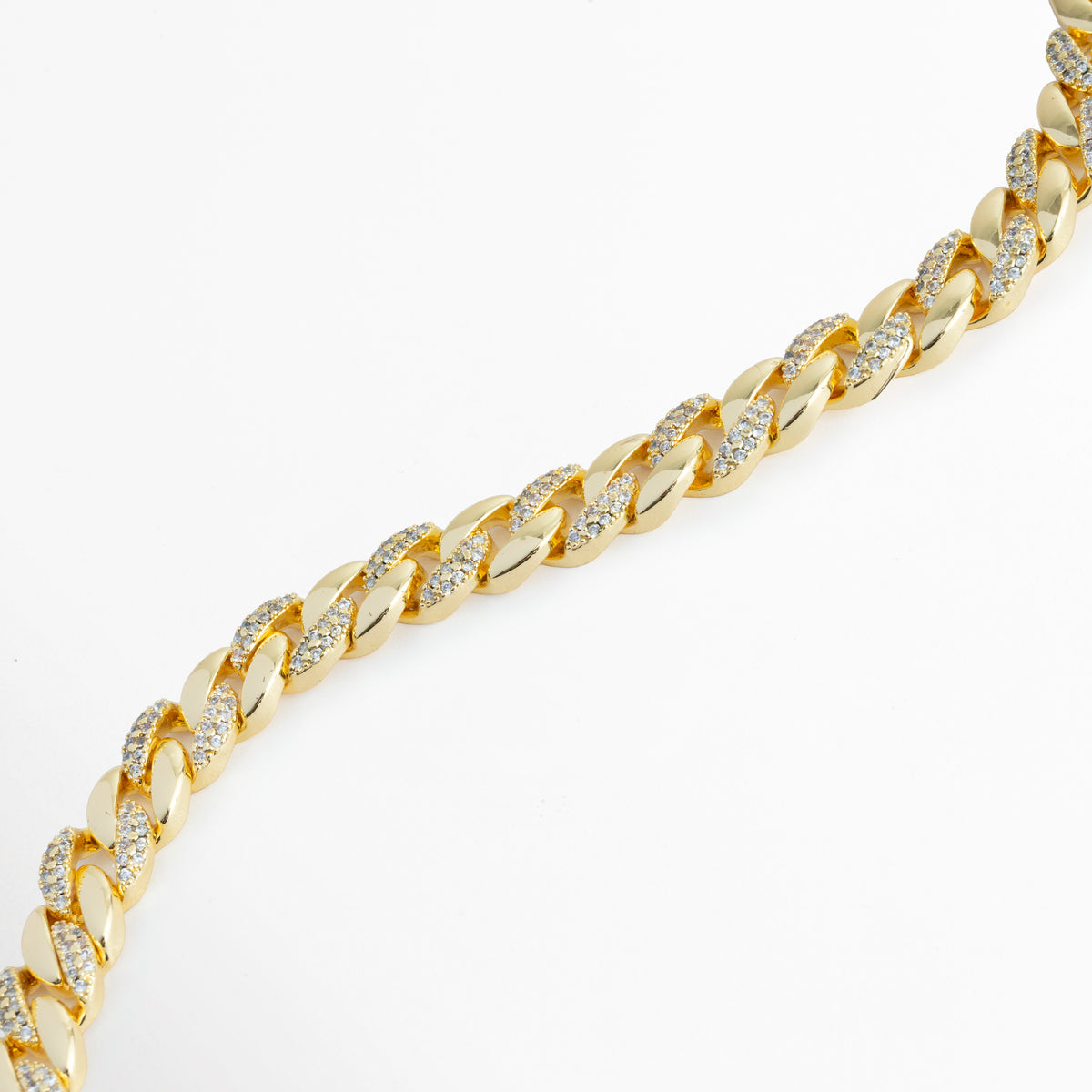 Vista en curva suave de la Pulsera Brock destacando la fluidez de los eslabones cubanos y el brillo de las circonias tipo CZ, Acercamiento a la textura entrelazada y al acabado enchapado en oro 18K de la cadena de 0.6 cm de ancho, Toma en diagonal que resalta los reflejos del baño dorado combinados con el pavé de pedrería cristalina, Muestra del perfil aplanado y ergonómico de los eslabones de estilo barbada sobre fondo blanco.