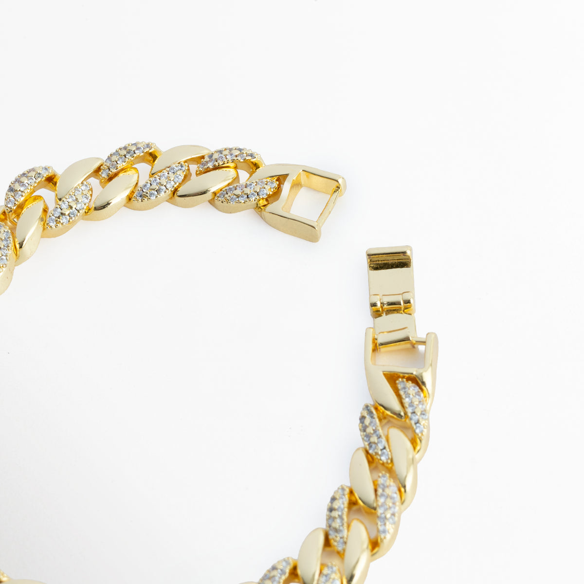 Acercamiento al broche plegable tipo reloj enchapado en oro 18K de la Pulsera Brock abierta, Vista macro del mecanismo de cierre de presión seguro integrado a los eslabones cubanos, Detalle de la terminación pulida del broche y la alineación del pavé de circonias CZ sobre fondo claro, Muestra del sistema de sujeción metálico de alta resistencia en tono oro brillante