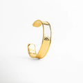 Brazalete rígido Velaris de acero inoxidable con baño de oro y acabado martillado orgánico, Pulsera ancha tipo cuff dorada con textura de relieve artesanal sobre fondo blanco, Joyería de acero inoxidable: brazalete dorado con bordes redondeados y acabado brillante, Detalle de pulsera Velaris con textura irregular que captura la luz, estilo minimalista audaz, Brazalete abierto ajustable enchapado en oro con 1.5 cm de ancho y diseño contemporáneo.