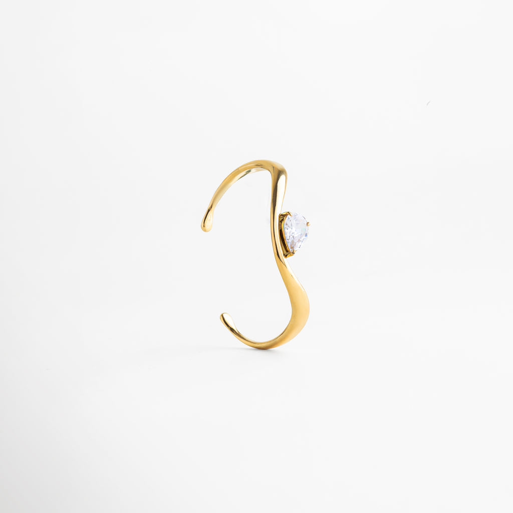 Pulsera tipo cuff ajustable en acero inoxidable 304 con baño de oro 18K y zirconia, Pulsera abierta dorada con zirconia central, diseño elegante y moderno, Pulsera rígida con acabado en oro 18K y piedra zirconia brillante, Pulsera minimalista ajustable con diseño fluido y zirconia incrustada, Pulsera contemporánea dorada con forma orgánica y detalle de zirconia