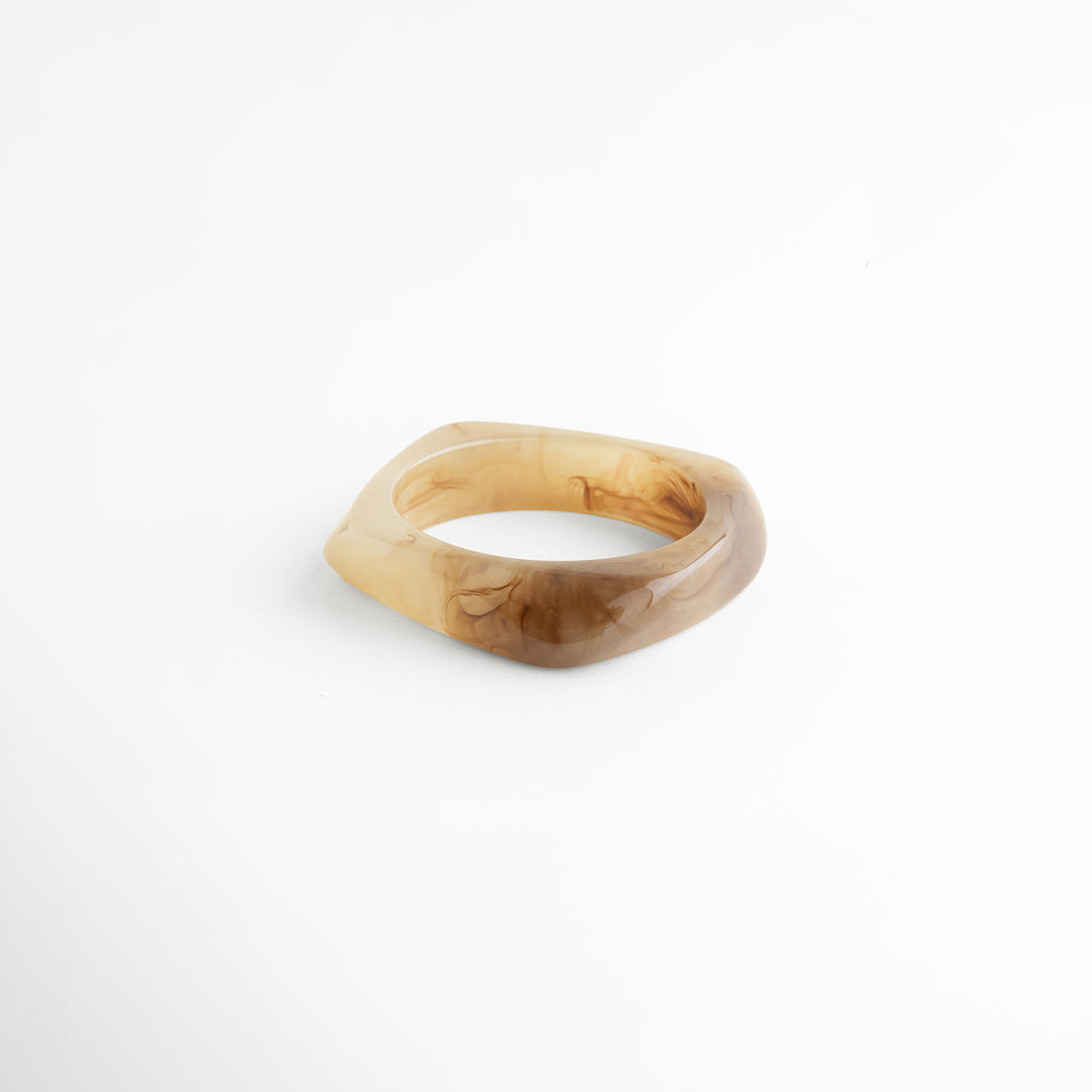 Vista frontal de pulsera de resina con diseño grueso y acabado brillante, Pulsera rígida con efecto marmoleado en tonos dorados, Pulsera elegante de resina con estilo minimalista moderno, Pulsera de resina translúcida con diseño sólido y sofisticado, Detalle frontal de pulsera chunky con acabado pulido