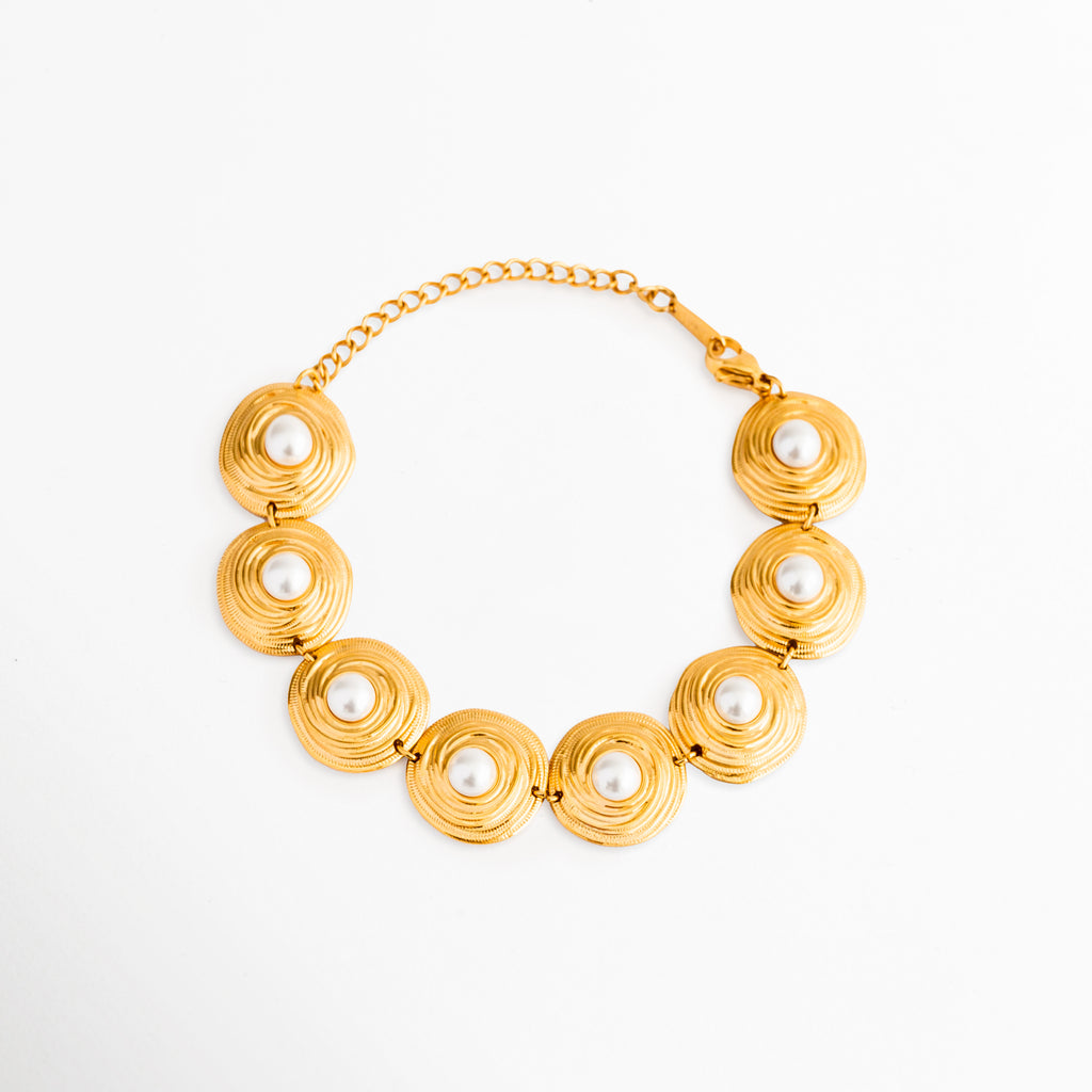 Pulsera Khalira de eslabones circulares dorados con incrustaciones de perlas blancas, Pulsera de acero inoxidable chapada en oro de 18K con detalles de perlas de alto brillo, Joyería elegante: pulsera dorada con dijes redondos y perlas centrales sobre fondo blanco, Pulsera ajustable de eslabones planos de oro con perlas clásicas de imitación, Vista completa de la pulsera Khalira mostrando su cadena extensoria y broche.