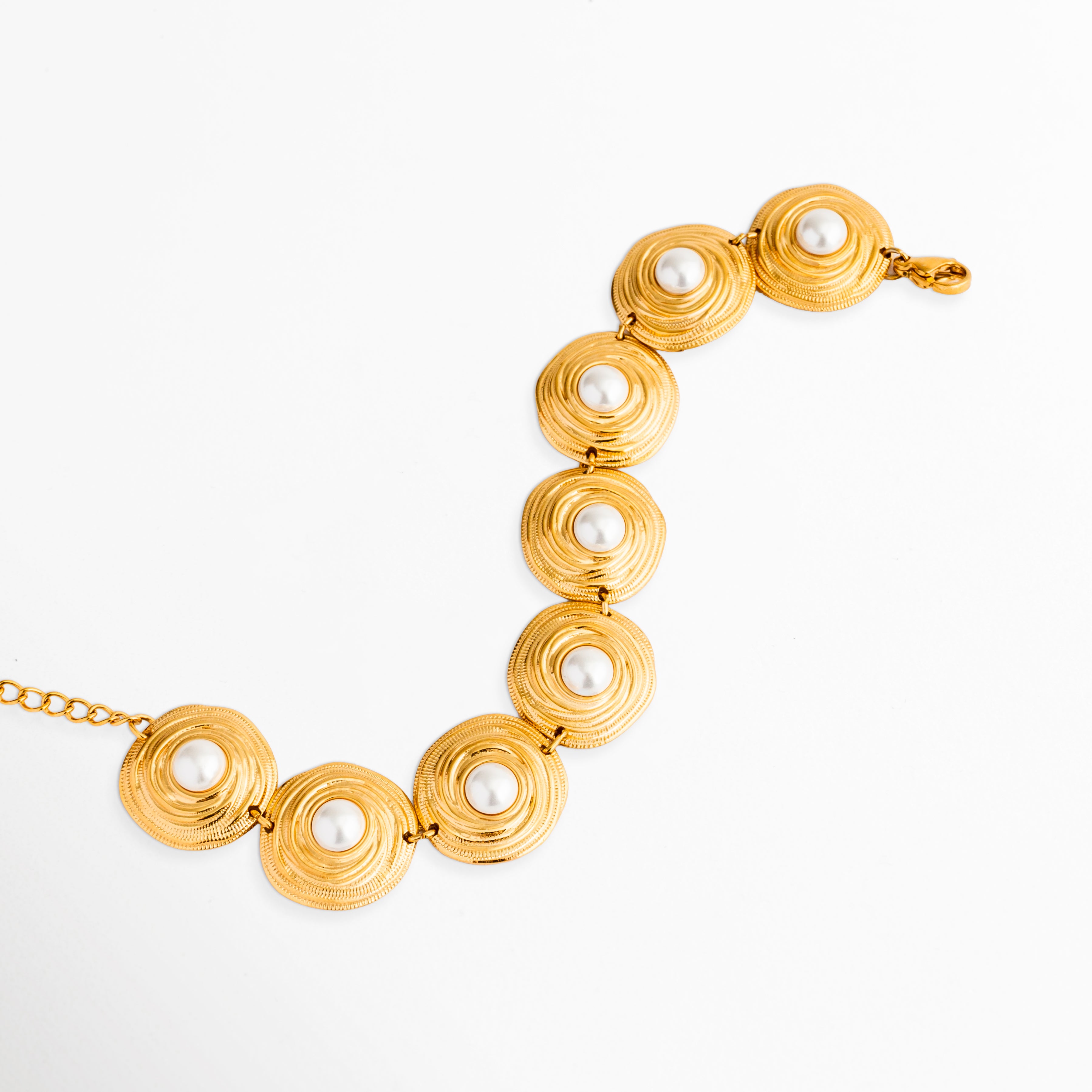 Primer plano de los eslabones circulares con relieve de la pulsera dorada Khalira, Detalle de las perlas de alto brillo incrustadas en los dijes redondos de oro, Textura y acabado del enchapado en oro de 18K en los eslabones de la pulsera, Close-up de pulsera de acero inoxidable dorada mostrando el diseño de las perlasEnfoque en el patrón curvo de dijes circulares dorados y perlas blancas.