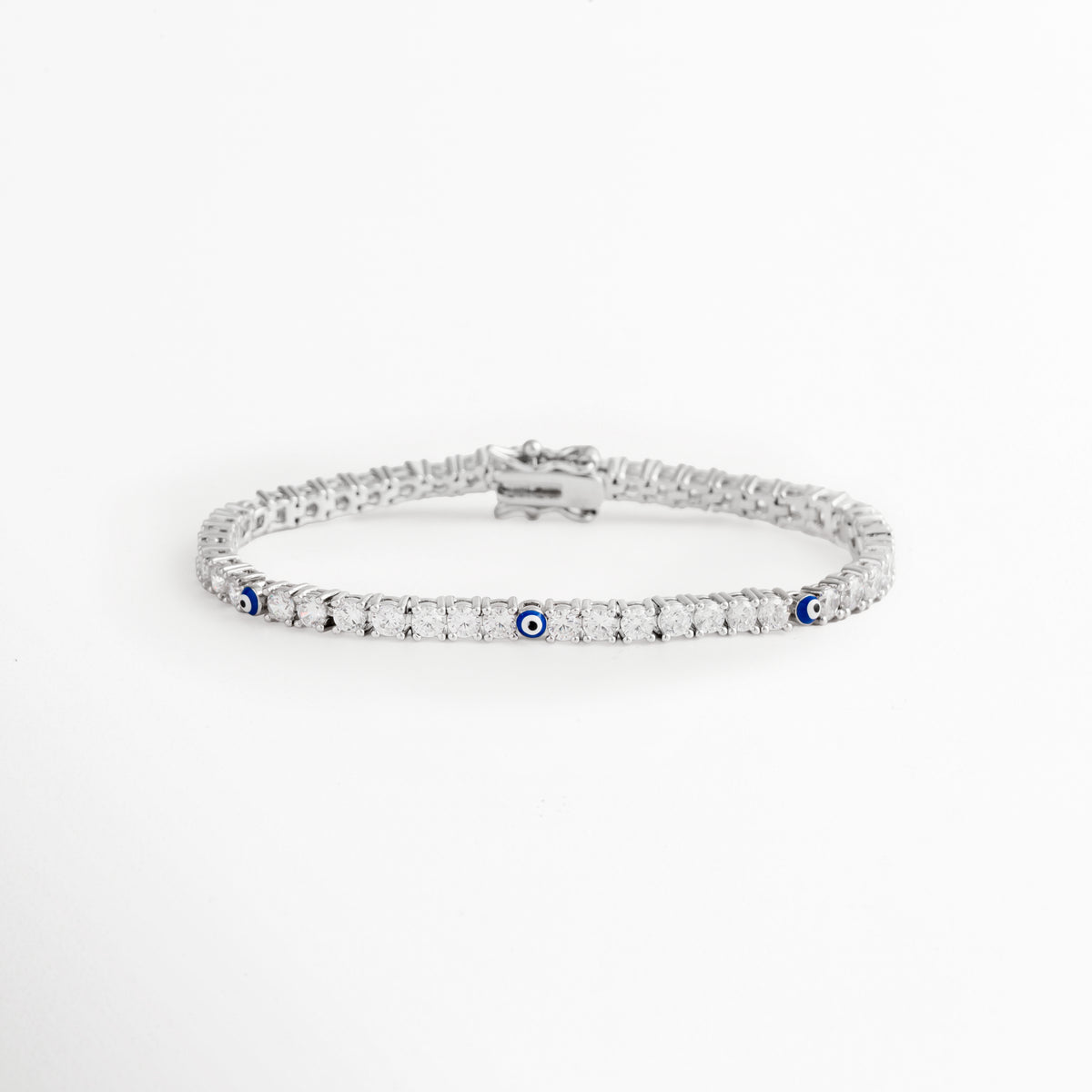 Pulsera tennis enchapada en oro blanco de 17 cm con circonias cristalinas y pequeños detalles de ojo turco azul, vista superior sobre fondo blanco, Vista de frente de pulsera estilo tennis plateada de 0.3 cm de ancho con engaste continuo de pedrería y amuletos de ojo turco, Plano general de pulsera de circonias transparentes con acentos de protección de ojo turco azul en acabado plateado, Pulsera tennis plateada de cobre enchapado en oro blanco con pedrería brillante