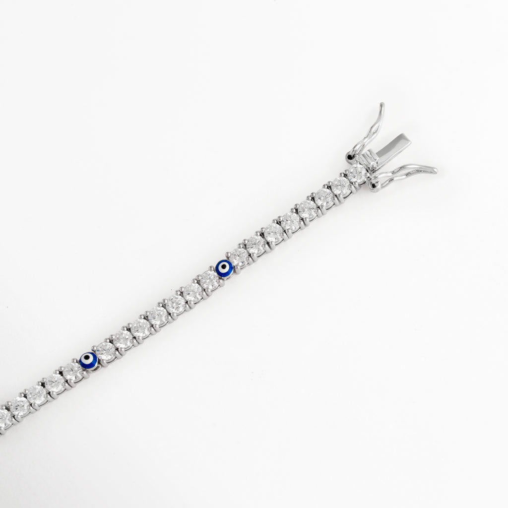 Acercamiento al broche de caja con doble traba de seguridad en pulsera tennis enchapada en oro blanco, Vista macro del sistema de cierre de alta joyería para pulsera delgada de circonias sobre fondo blanco, Detalle del mecanismo de ajuste seguro y terminación metálica pulida de la pulsera tennis de 17 cm, Muestra del broche de seguridad tipo joyería fina en pulsera de circonias y ojo turco.