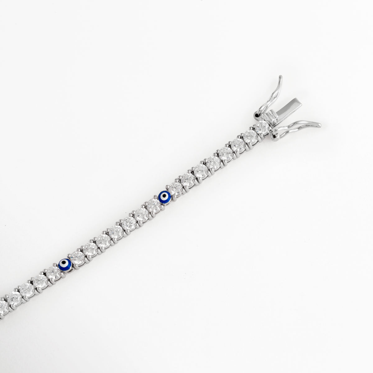 Acercamiento al broche de caja con doble traba de seguridad en pulsera tennis enchapada en oro blanco, Vista macro del sistema de cierre de alta joyería para pulsera delgada de circonias sobre fondo blanco, Detalle del mecanismo de ajuste seguro y terminación metálica pulida de la pulsera tennis de 17 cm, Muestra del broche de seguridad tipo joyería fina en pulsera de circonias y ojo turco.