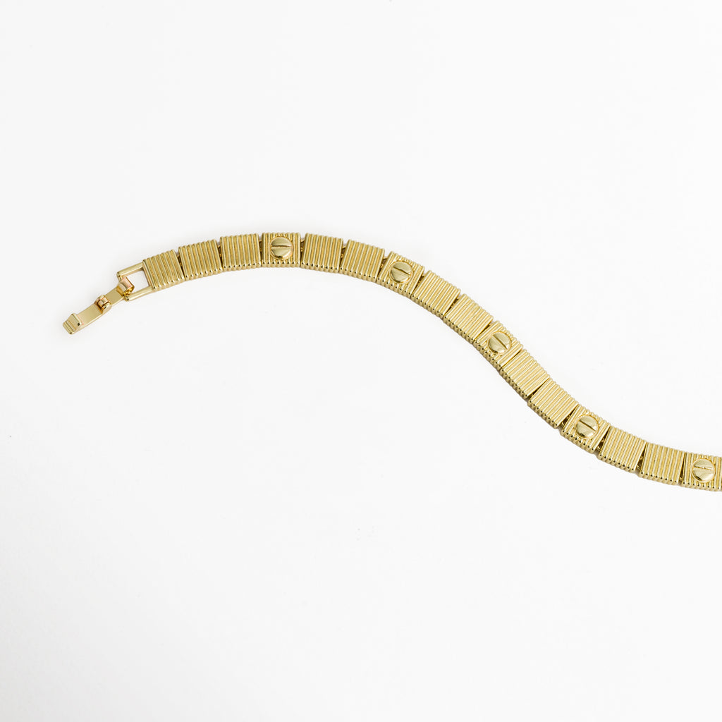 Vista en curva suave de la Pulsera Golden Alba destacando la articulación fluida entre eslabones acanalados, Acercamiento a la secuencia intercalada de placas con textura estriada y círculos grabados en tono dorado, Muestra del brillo del acabado enchapado en oro 18K en el perfil y reverso del brazalete, Plano medio de la pulsera dorada de 0.6 cm de ancho mostrando la flexibilidad de sus eslabones.