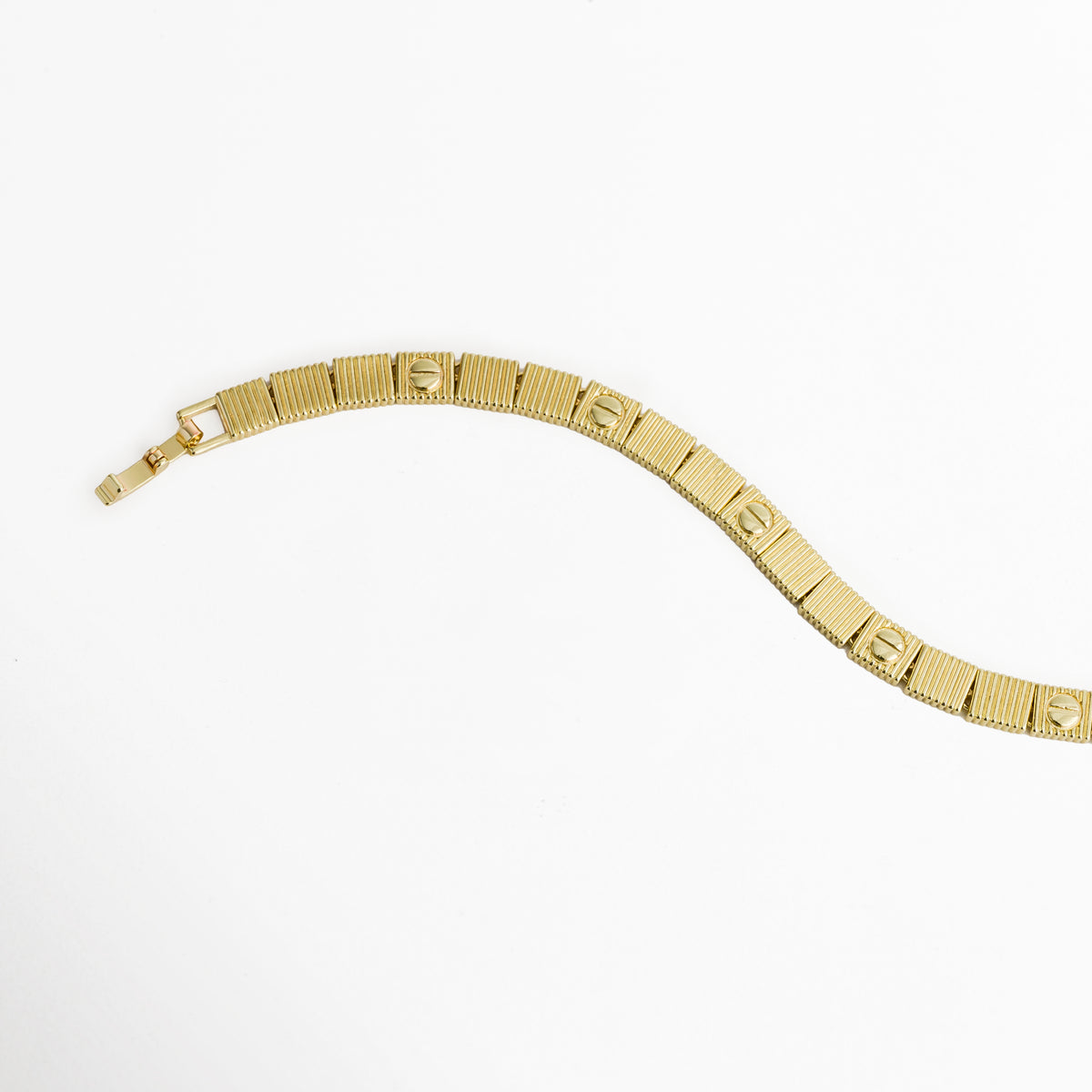 Vista en curva suave de la Pulsera Golden Alba destacando la articulación fluida entre eslabones acanalados, Acercamiento a la secuencia intercalada de placas con textura estriada y círculos grabados en tono dorado, Muestra del brillo del acabado enchapado en oro 18K en el perfil y reverso del brazalete, Plano medio de la pulsera dorada de 0.6 cm de ancho mostrando la flexibilidad de sus eslabones.