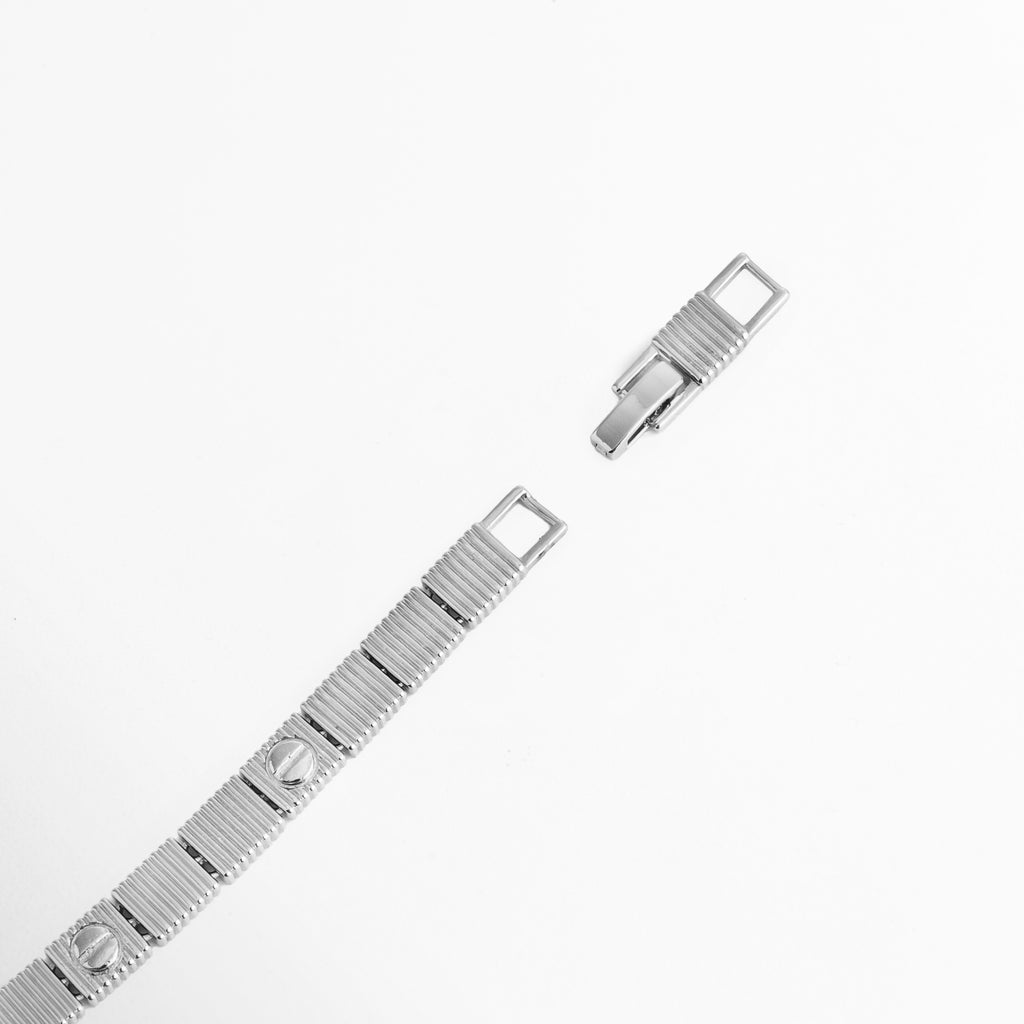 Acercamiento al broche plegable desplegado y eslabón de extensión desmontable de la Pulsera Silver Alba, Vista macro del sistema de cierre de broche tipo reloj en acero inoxidable enchapado en oro blanco 18K, Detalle de las placas cuadradas con motivo de tornillo y el mecanismo de sujeción ajustable sobre fondo blanco, Muestra de la extensión desmontable de 3 cm que permite ajustar la pulsera de 17 cm a 20 cm.