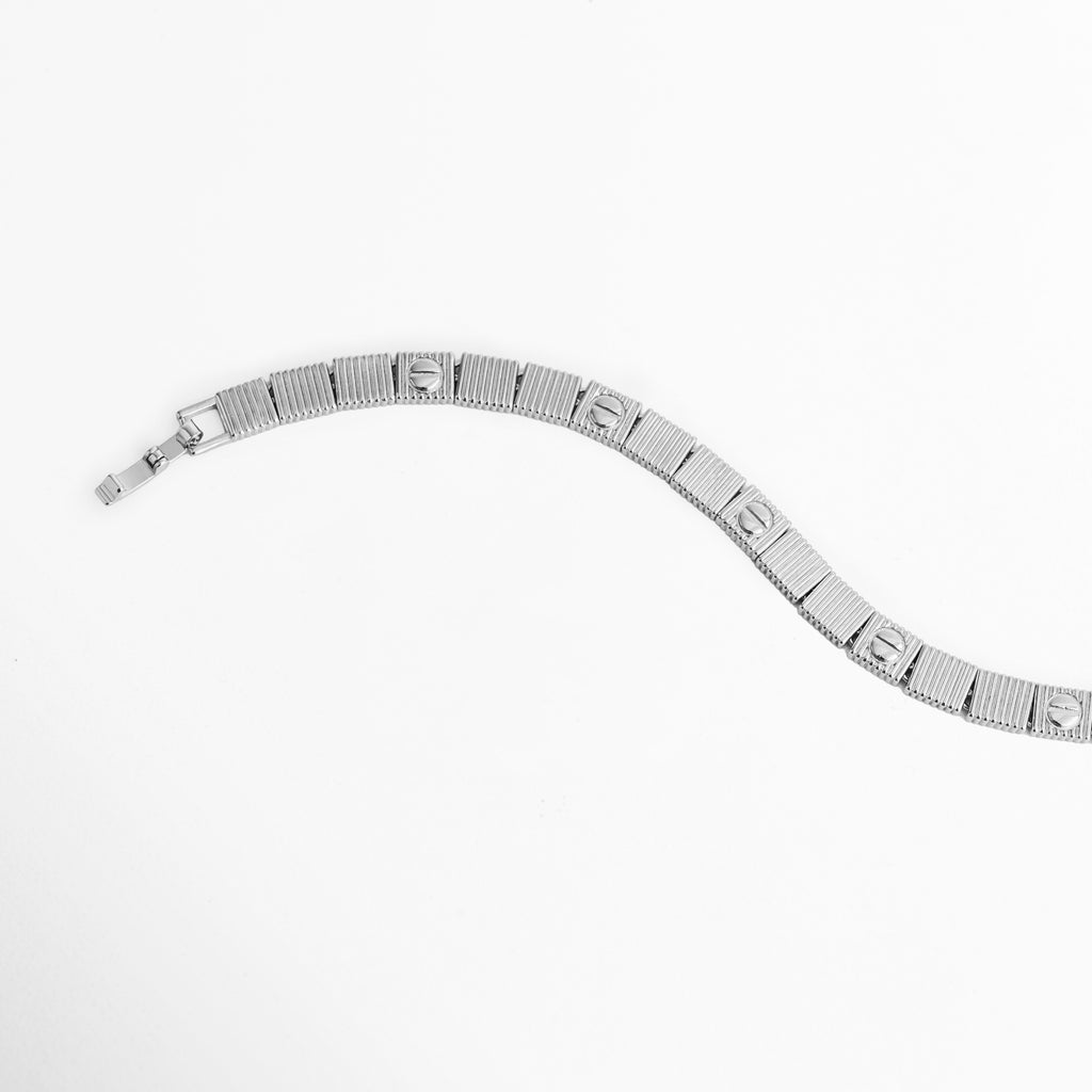 Vista en curva suave de la Pulsera Silver Alba destacando la articulación fluida entre eslabones acanalados,  Acercamiento a la secuencia intercalada de placas con textura estriada y círculos grabados en tono plateado, Muestra del brillo del acabado enchapado en oro blanco 18K en el perfil y reverso del brazalete, Plano medio de la pulsera plateada de 0.6 cm de ancho mostrando la flexibilidad de sus eslabones.