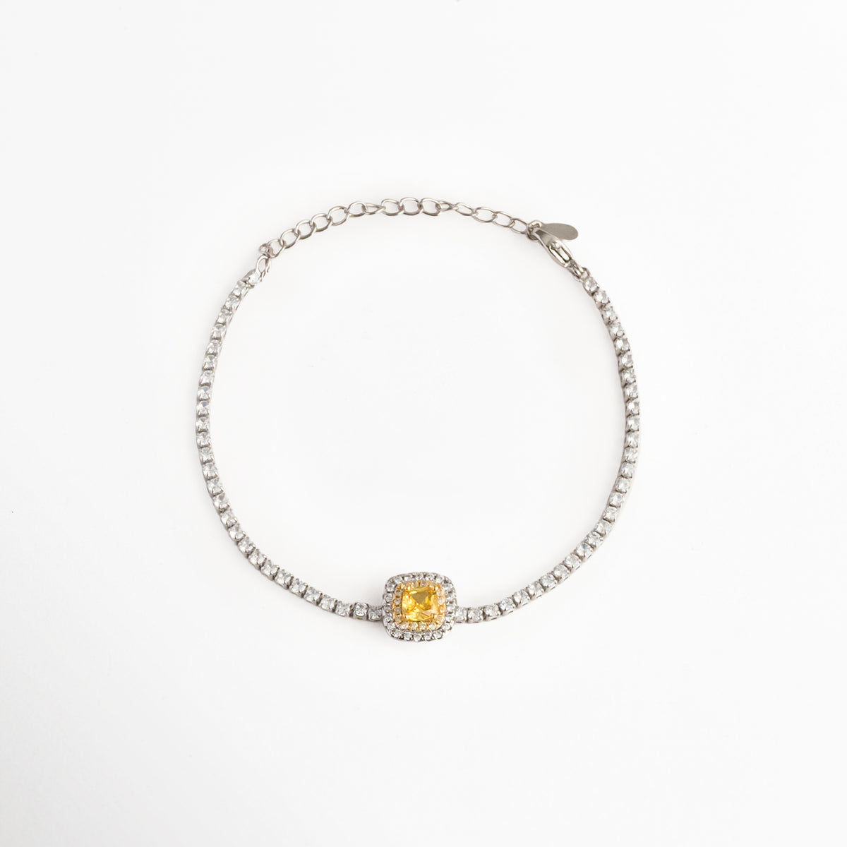 Pulsera Yellow estilo tennis enchapada en oro blanco con circonia central de corte cojín en color amarillo canario enmarcada por un halo brillante, vista superior sobre fondo blanco, Vista de frente de pulsera plateada delgada con gema central de circonia amarilla cuadrada y halo de pedrería transparente, Plano general de pulsera estilo tennis enchapada en oro blanco con gema amarilla en el centro y cadena de extensión, Pulsera Yellow de cobre enchapado en oro