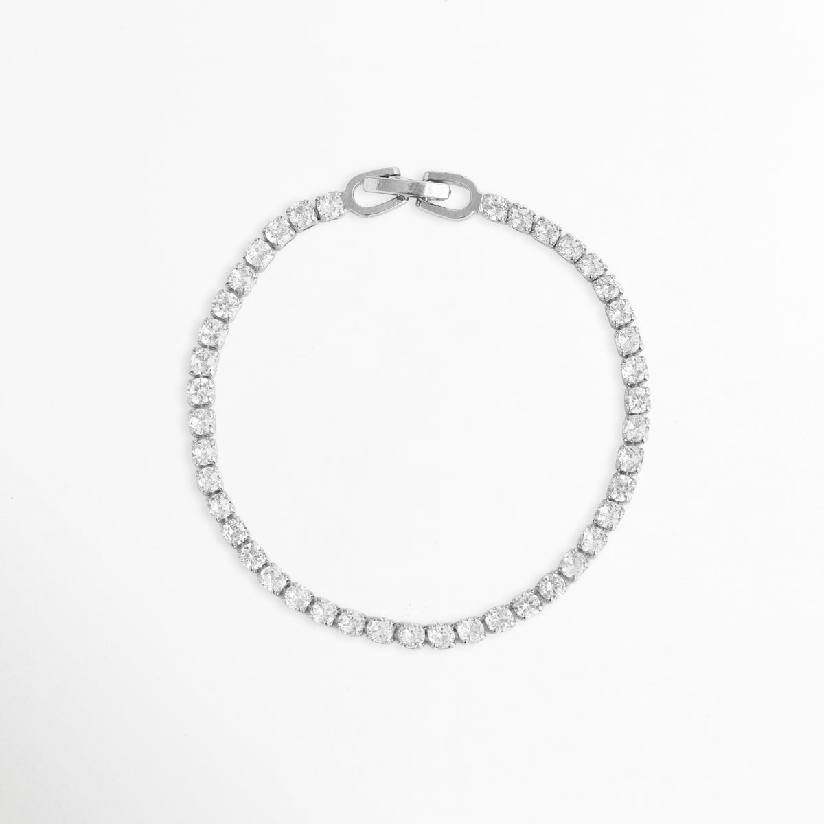 Pulsera Tennis Elora de cobre enchapada en plata de 17 cm con hileras continuas de circonias transparentes de 0.3 cm de ancho, vista superior en círculo sobre fondo blanco, Vista de frente de pulsera estilo tennis plateada en silueta circular con pedrería cristalina de corte brillante engastada, Plano general de brazalete flexible de hileras continuas de circonias en acabado plata sobre fondo neutro, Pulsera Tennis Elora destacando el brillo helado
