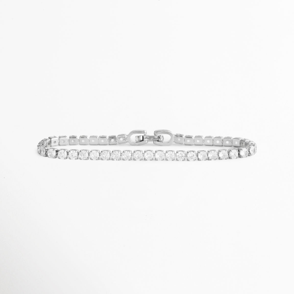 Vista horizontal en línea recta de la Pulsera Tennis Elora extendida mostrando el broche plegable y el perfil delgado de 0.3 cm, Acercamiento a la tira continua de circonias transparentes enchapadas en plata de 17 cm de longitud, Toma en perspectiva que resalta la flexibilidad de la cadena articulada y el brillo constante de la pedrería, Muestra de la simetría de los engastes metálicos plateados en la pulsera tennis sobre fondo blanco.