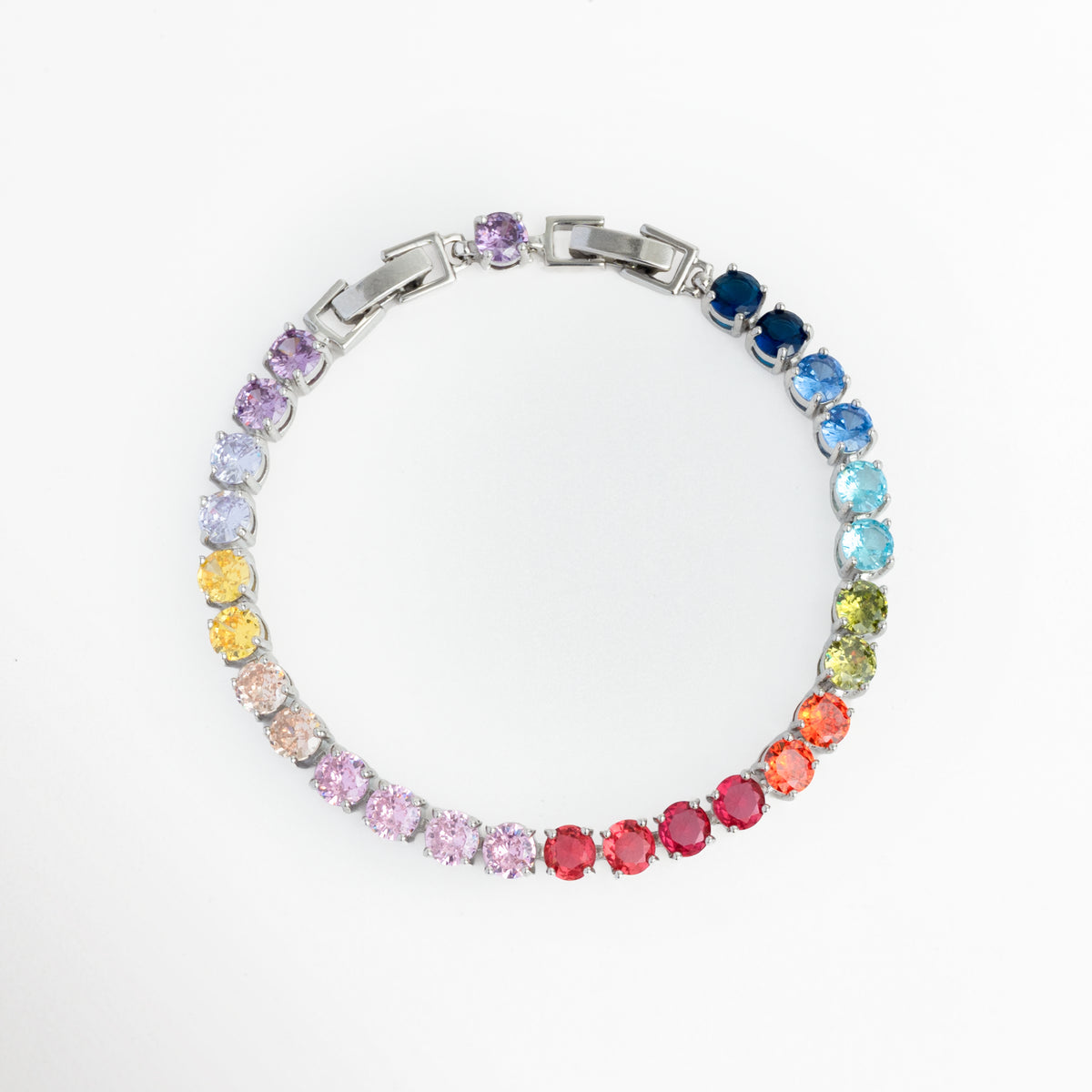 Pulsera Tennis Bracelet Rainbow enchapada en rodio con hileras de circonias circulares en degradé multicolor de arcoíris, vista frontal en círculo sobre fondo blanco, Brazalete estilo tennis de 17 cm más extensión de 2.5 cm con gemas de circonia en tonos azul, verde, amarillo, rosa y rojo, Vista de frente de pulsera de cobre enchapada en rodio con bisel de gemas cristalinas de colores en degradé, Pulsera estilo riviera o tennis multicolor de 0.5 cm de ancho.