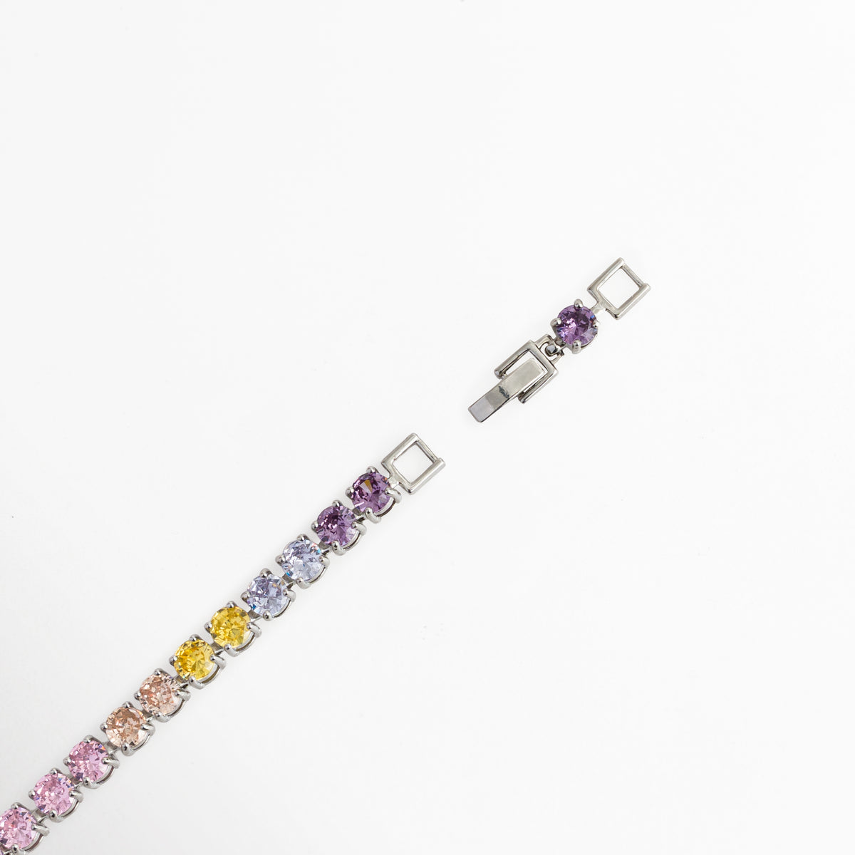 Detalle del cierre desplegable de broche de escala de la pulsera Tennis Bracelet Rainbow mostrando el broche abierto y la extensión. Vista de cerca del mecanismo de cierre plegable enchapado en rodio con circonia violeta integrada en el extensor, Acercamiento al broche metálico de seguridad y ajuste de longitud de la pulsera tennis multicolor, Detalle del broche desplegable plateado sobre fondo blanco en toma diagonal.