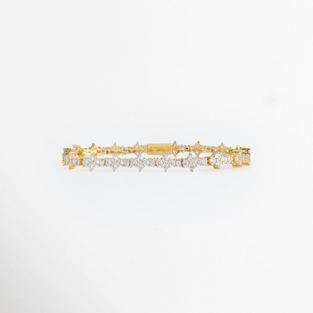Pulsera Golden Musa enchapada en oro con motivos florales de cuatro pétalos de circonia transparente, vista frontal sobre fondo blanco, Vista de frente de brazalete dorado de 0.7 cm de ancho con secuencia continua de rosetas y flores de pedrería brillante, Plano general de pulsera articulada de cobre enchapada en oro con eslabones florales de circonias cristalinas, Pulsera Golden Musa mostrando la simetría de sus motivos estelares y florales en tono oro de 18 cm 