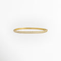Pulsera Golden Liore rígida de cobre enchapado en oro con pavé frontal de micro-circonias transparentes de 0.3 cm de ancho, vista de frente, Vista frontal de brazalete rígido tipo caña dorada con incrustación continua de circonias cristalinas y bisagras invisibles, Plano general de pulsera rígida ovalada de 6 cm de diámetro interno enchapada en oro con brillo de pedrería, Pulsera Golden Liore destacando el resplandor de la micro-pedrería engastada en la mitad fronta