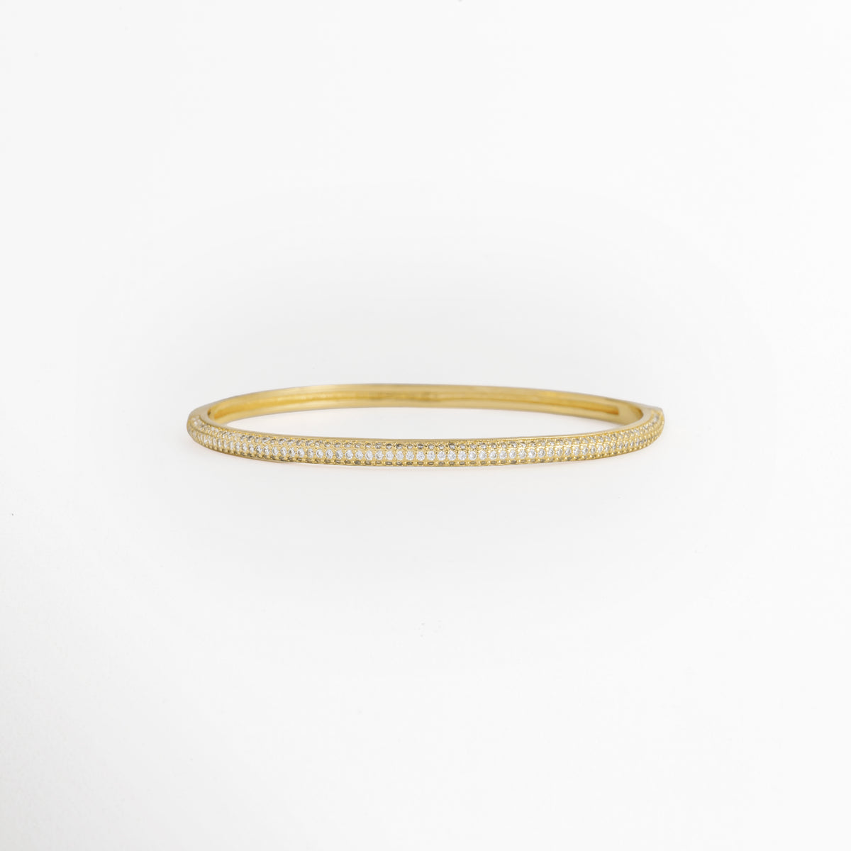 Pulsera Golden Liore rígida de cobre enchapado en oro con pavé frontal de micro-circonias transparentes de 0.3 cm de ancho, vista de frente, Vista frontal de brazalete rígido tipo caña dorada con incrustación continua de circonias cristalinas y bisagras invisibles, Plano general de pulsera rígida ovalada de 6 cm de diámetro interno enchapada en oro con brillo de pedrería, Pulsera Golden Liore destacando el resplandor de la micro-pedrería engastada en la mitad fronta