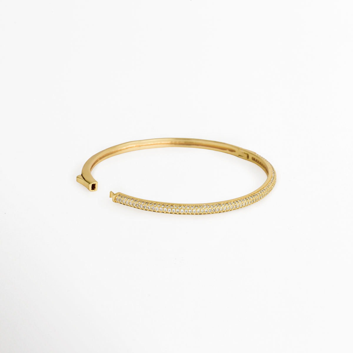 Vista en ángulo de la Pulsera Golden Liore abierta mostrando el mecanismo de bisagra lateral y cierre de presión, Acercamiento al sistema de apertura del brazalete rígido dorado de 6 cm de diámetro interno, Toma en perspectiva que resalta la estructura interna pulida del brazalete de cobre enchapado en oro, Muestra del mecanismo de sujeción práctico para una fácil colocación sobre la muñeca.   