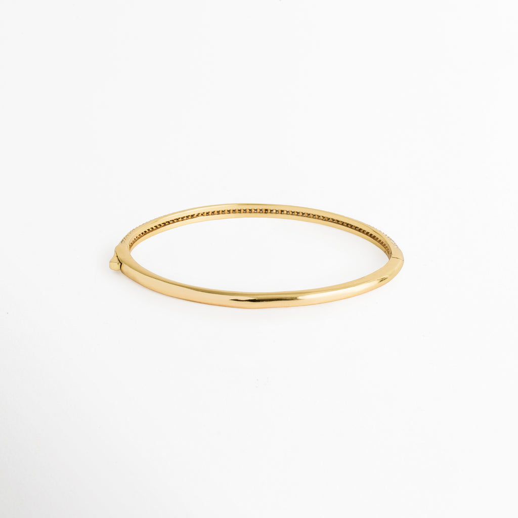 Vista de la cara posterior de la Pulsera Golden Liore en acabado dorado liso de alto pulido espejo, Acercamiento al reverso de la caña rígida de cobre enchapada en oro mostrando su superficie limpia y brillante, Toma de perfil posterior del brazalete cerrado de 6 cm de diámetro interno, Muestra del acabado pulido impecable en el reverso del brazalete tipo bangle. 