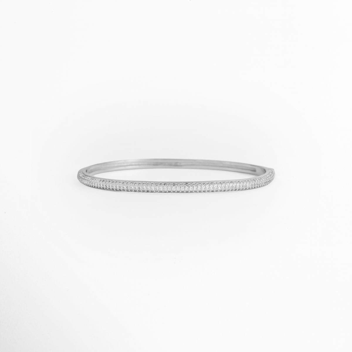 Pulsera Silver Liore rígida de cobre enchapado en oro blanco con pavé frontal de micro-circonias transparentes de 0.3 cm de ancho, vista de frente, Vista frontal de brazalete rígido tipo caña plateada con incrustación continua de circonias cristalinas y bisagras invisibles, Plano general de pulsera rígida ovalada de 6 cm de diámetro interno enchapada en oro blanco con brillo de pedrería, Pulsera Silver Liore destacando el resplandor de la micro-pedrería engastada 