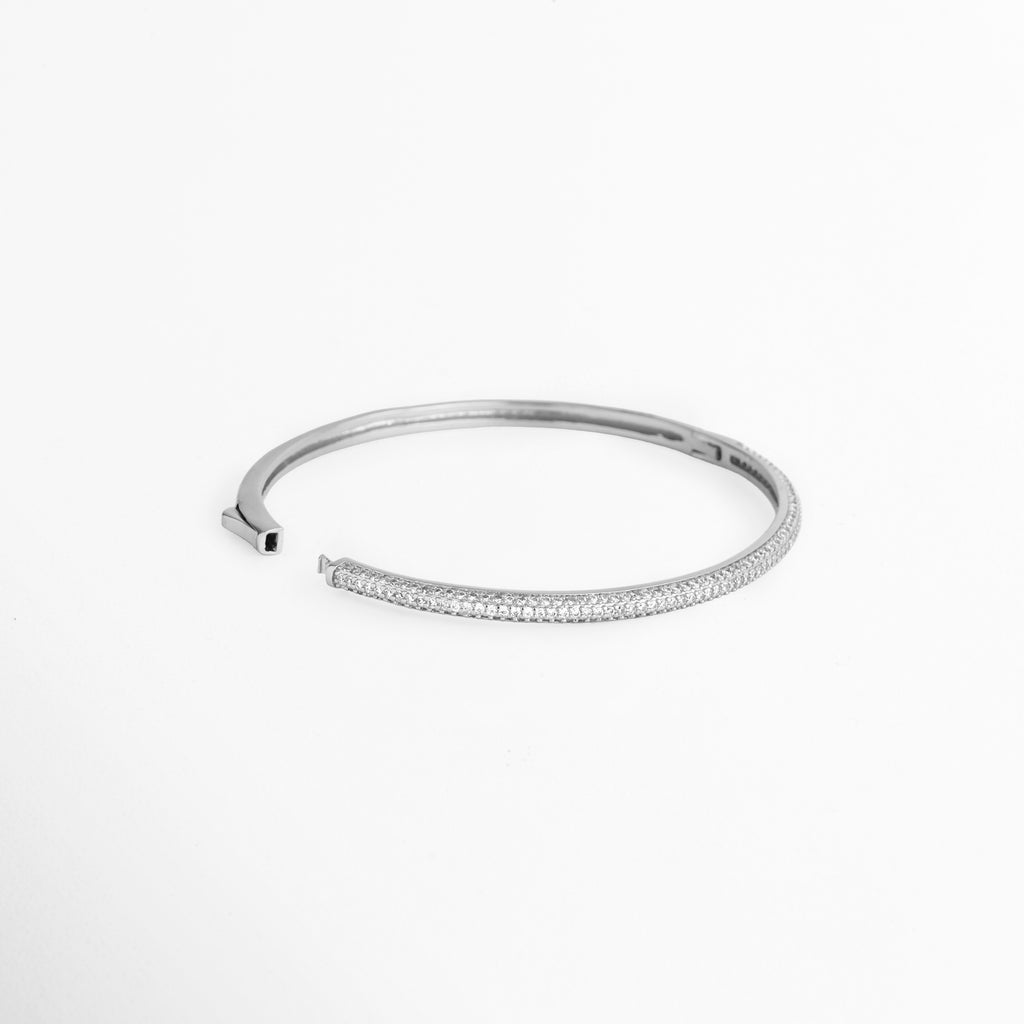 Vista en ángulo de la Pulsera Silver Liore abierta mostrando el mecanismo de bisagra lateral y cierre de presión,  Acercamiento al sistema de apertura del brazalete rígido plateado de 6 cm de diámetro interno, Toma en perspectiva que resalta la estructura interna pulida del brazalete de cobre enchapado en oro blanco, Muestra del mecanismo de sujeción práctico para una fácil colocación sobre la muñeca.   