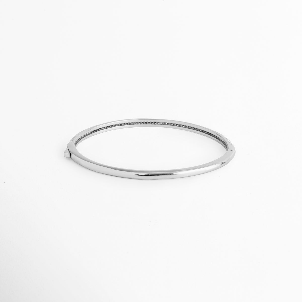 Vista de la cara posterior de la Pulsera Silver Liore en acabado plateado liso de alto pulido espejo, Acercamiento al reverso de la caña rígida de cobre enchapada en oro blanco mostrando su superficie limpia y brillante, Toma de perfil posterior del brazalete cerrado de 6 cm de diámetro interno, Muestra del acabado pulido impecable en el reverso del brazalete tipo bangle plateado
