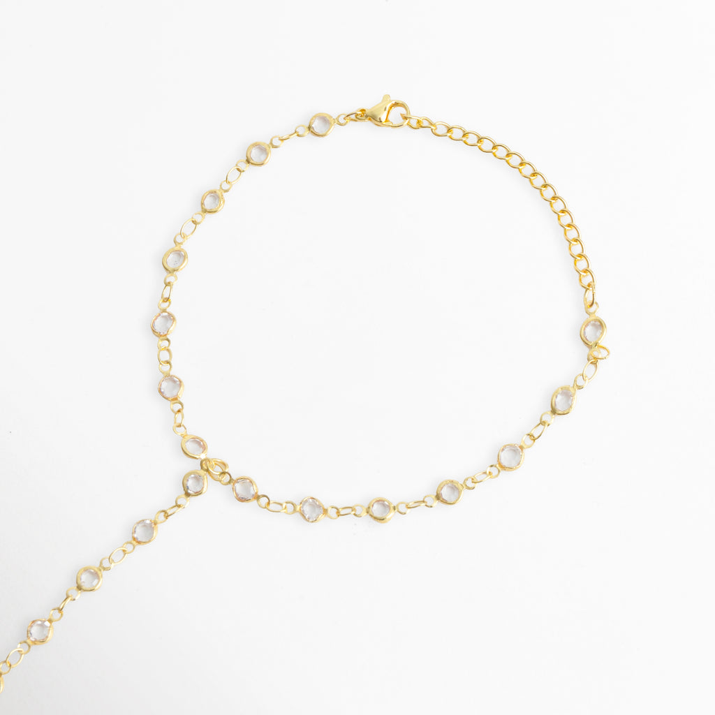 Vista de la sección de muñeca de la Pulsera Esclava Zayra mostrando la cadena de ajuste de 18 cm más 5 cm de extensión y el broche de langosta, Acercamiento al broche reasa/mosquetón dorado y la cadena de extensión para ajustar el diámetro de la muñeca, Toma que muestra el punto de bifurcación de la cadena con circonias hacia el dorso de la mano sobre fondo blanco, Muestra de la flexibilidad y el acabado brillante del baño dorado sobre la base de cobre.