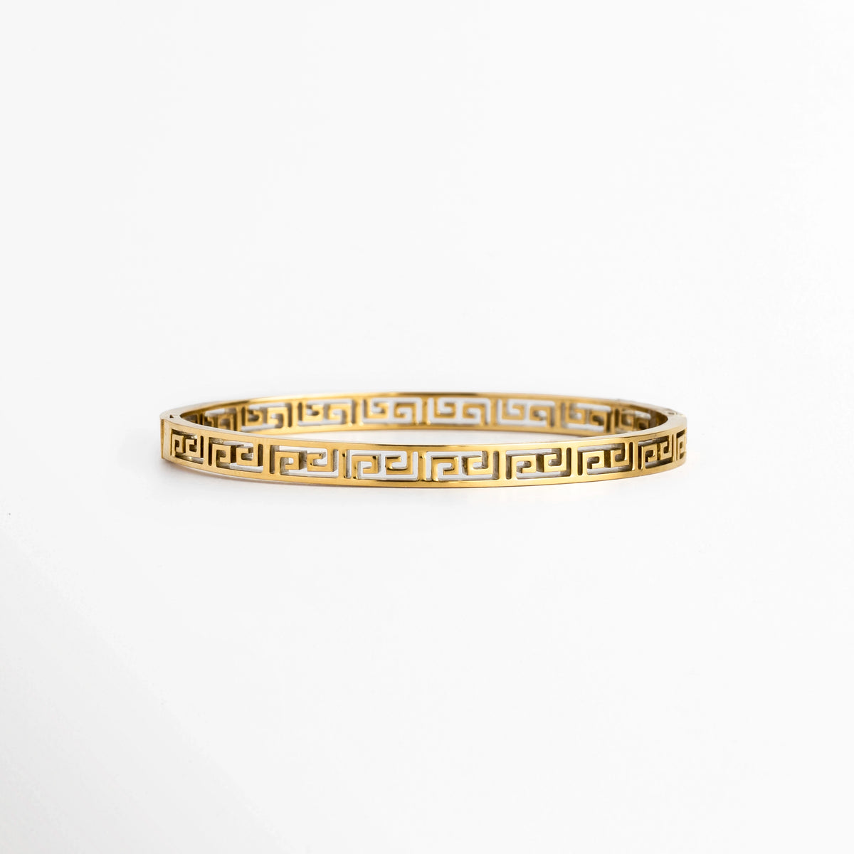 Pulsera Amani de acero de titanio enchapada en oro con diseño rígido de greca clásica o meandro calado de 0.5 cm de ancho, vista frontal sobre fondo blanco, Vista de frente de brazalete dorado de silueta ovalada con patrón geométrico estilo greca griega en calado continuo, Plano general de pulsera rígida en tono oro brillante con estructura arquitectónica de líneas labradas sobre fondo neutro, Pulsera Amani destacando el acabado de alto brillo sobre el acero