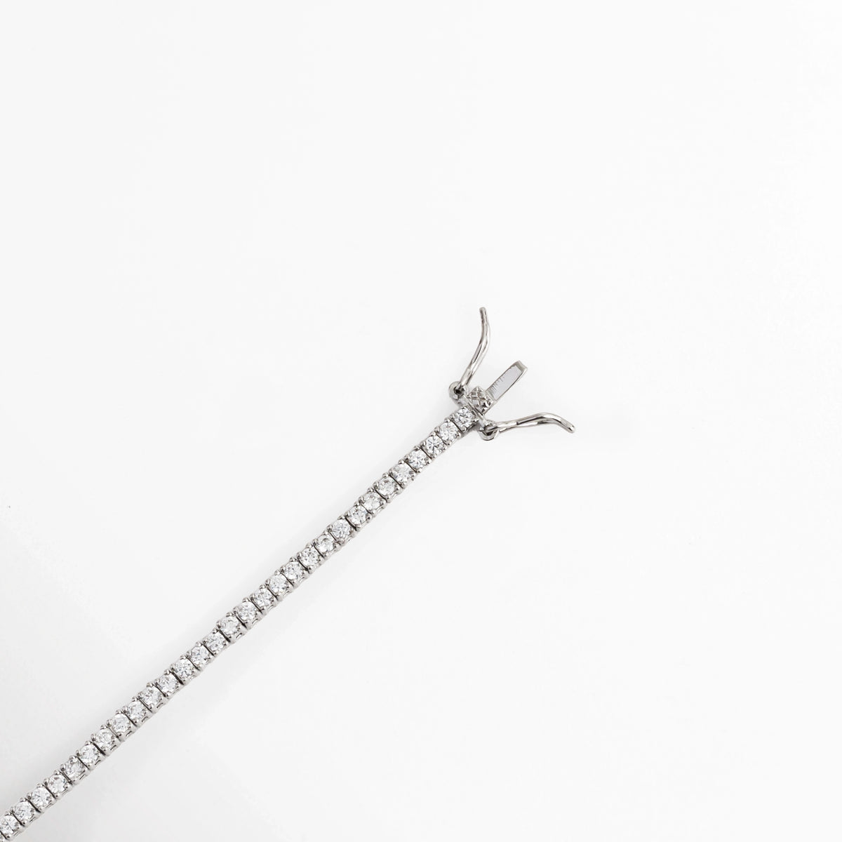 Acercamiento al broche de caja con doble pestillo de seguridad lateral enchapado en oro blanco de la Tennis Bracelet Beloved, Vista en diagonal del mecanismo de cierre tipo joyería en la pulsera tennis plateada, Detalle de la confección ultradelgada de 0.2 cm de ancho con engaste individual de micro-garras, Muestra del broche metálico abierto y las trabas de seguridad laterales sobre fondo claro.  