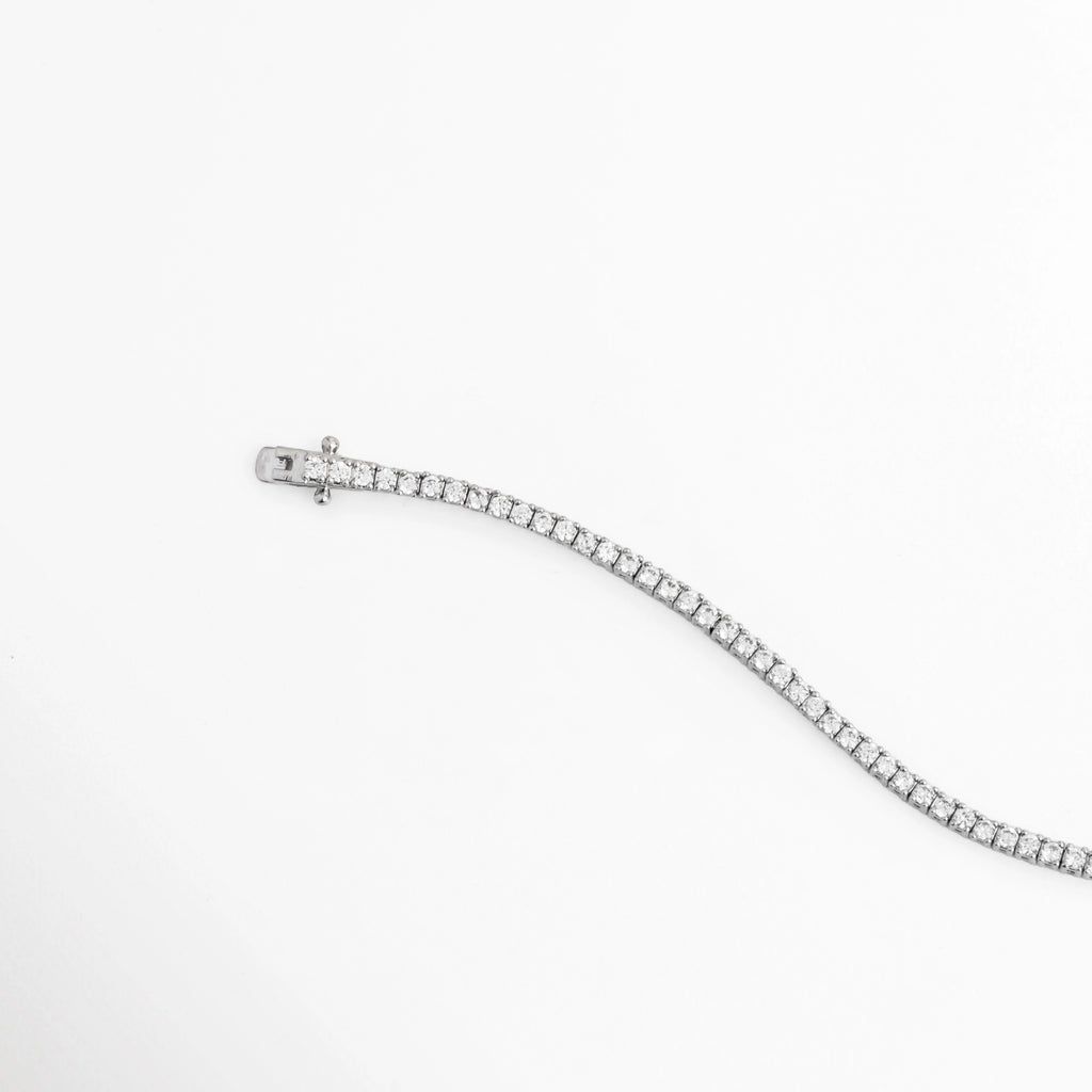 Vista en curva suave de la Tennis Bracelet Beloved destacando la flexibilidad y el brillo frío de las circonias transparentes, Acercamiento a la fluidez y articulación de los eslabones ultradelgados enchapados en oro blanco, Toma de perfil articulado que resalta el resplandor ininterrumpido de la pedrería al movimiento, Muestra de los destellos cristalinos sobre la fina tira de circonias de 18 cm de largo.