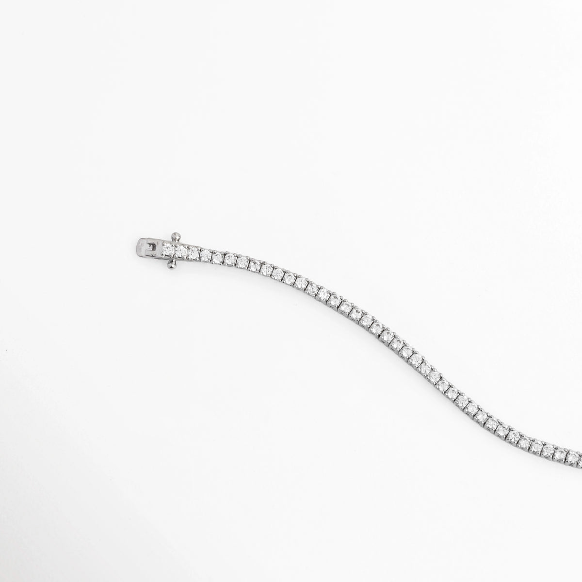 Vista en curva suave de la Tennis Bracelet Beloved destacando la flexibilidad y el brillo frío de las circonias transparentes, Acercamiento a la fluidez y articulación de los eslabones ultradelgados enchapados en oro blanco, Toma de perfil articulado que resalta el resplandor ininterrumpido de la pedrería al movimiento, Muestra de los destellos cristalinos sobre la fina tira de circonias de 18 cm de largo.