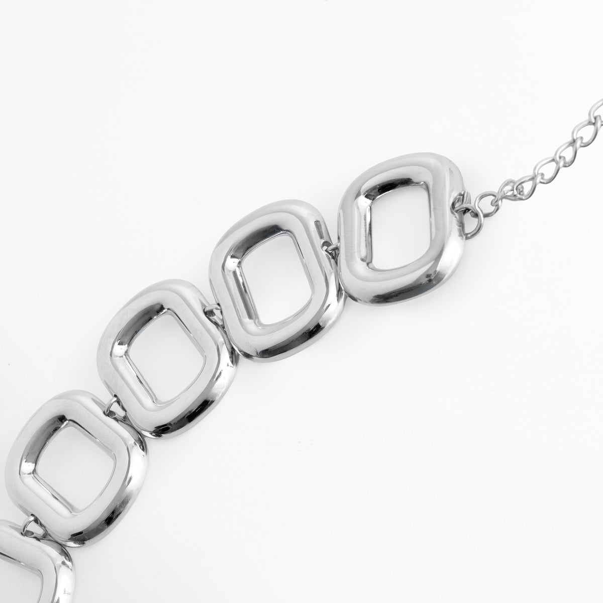 Acercamiento a la secuencia de eslabones cuadrados calados de la Pulsera Freire resaltando su grosor y volumen tridimensional, Vista en diagonal de los eslabones articulados enchapados en oro blanco con textura lisa de alto brillo espejo, Toma macro que muestra la unión impecable entre los módulos geométricos de 2.3 cm de ancho, Muestra del acabado metálico limpio y la estructura sólida de acero inoxidable.   
