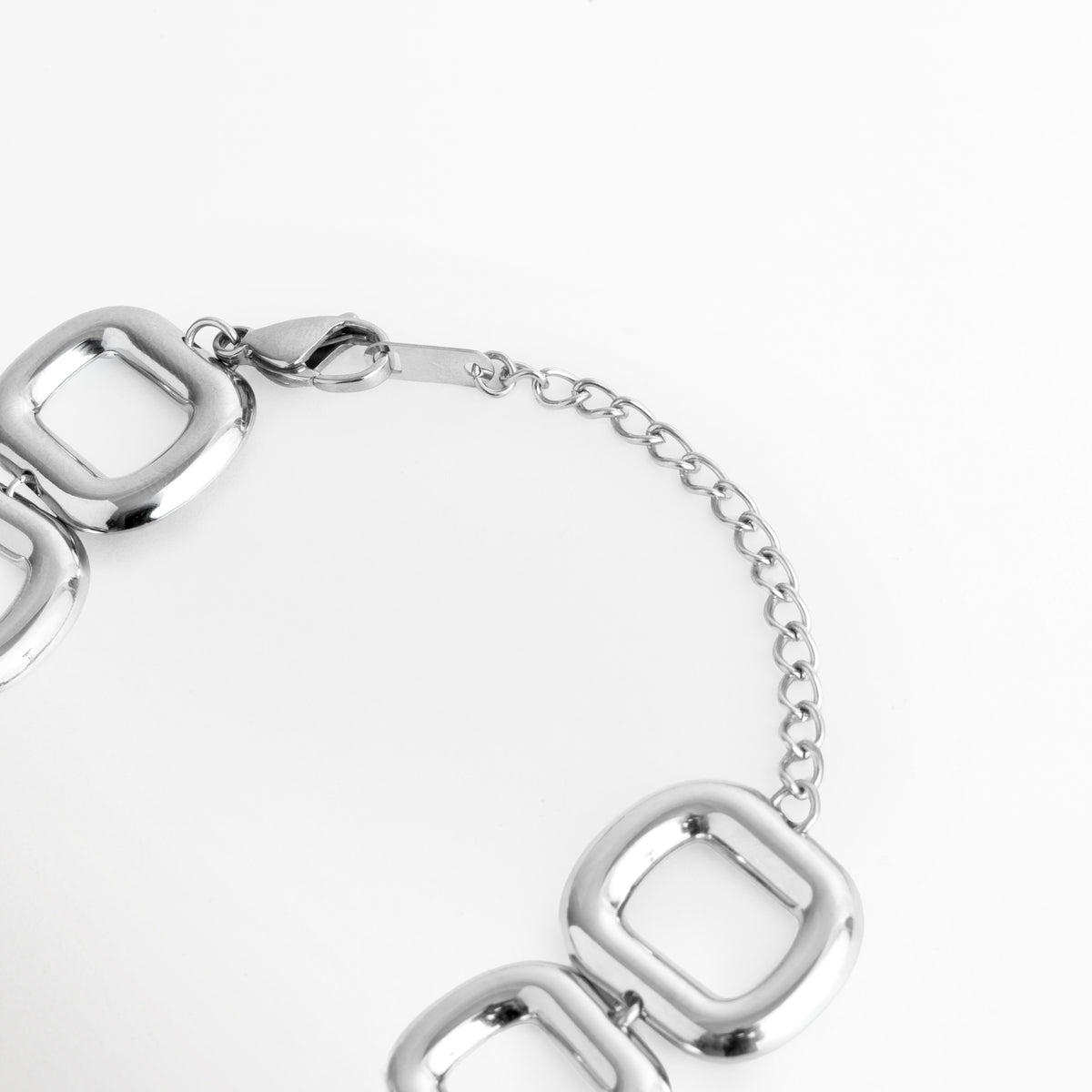 Acercamiento al broche de mosquetón y la cadena de extensión de 6 cm enchapada en oro blanco de la Pulsera Freire, Vista macro del sistema de sujeción ajustable y la medallón de marca sobre fondo blanco, Detalle de los eslabones de extensión que permiten adaptar la pulsera de 17 cm a 23 cm de longitud total, Muestra del mecanismo de cierre metálico seguro y duradero en acero inoxidable plateado. 