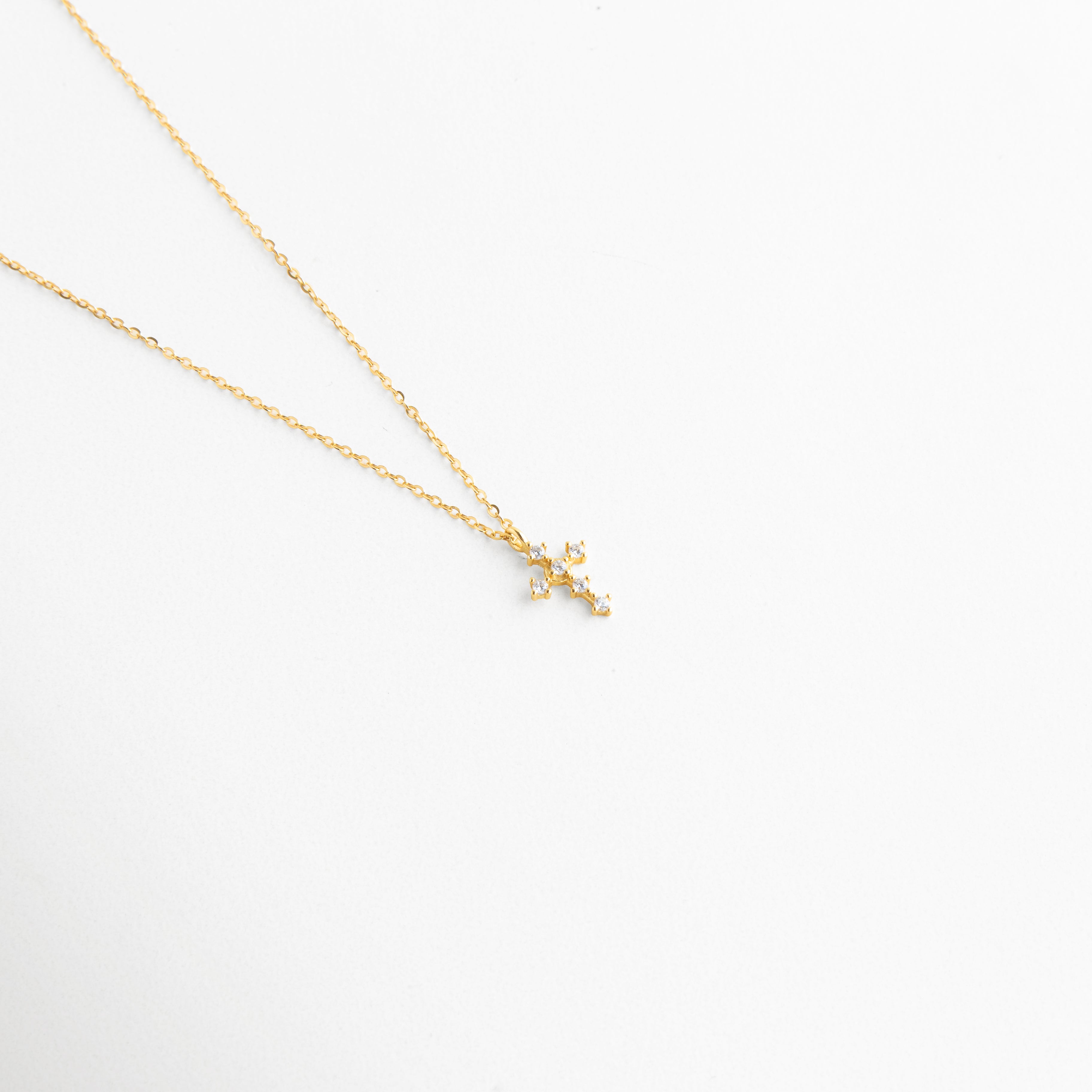 Vista inclinada de Collar Cruz Sagrada Dorada con dije de cruz y zirconias brillantes, Collar dorado con cruz pequeña en ángulo y acabado elegante en Oro 18K, Detalle del dije de cruz con zirconias en cadena fina dorada, Collar delicado con cruz brillante y diseño femenino en vista diagonal, Cadena dorada con dije de cruz decorado con zirconias en primer plano.