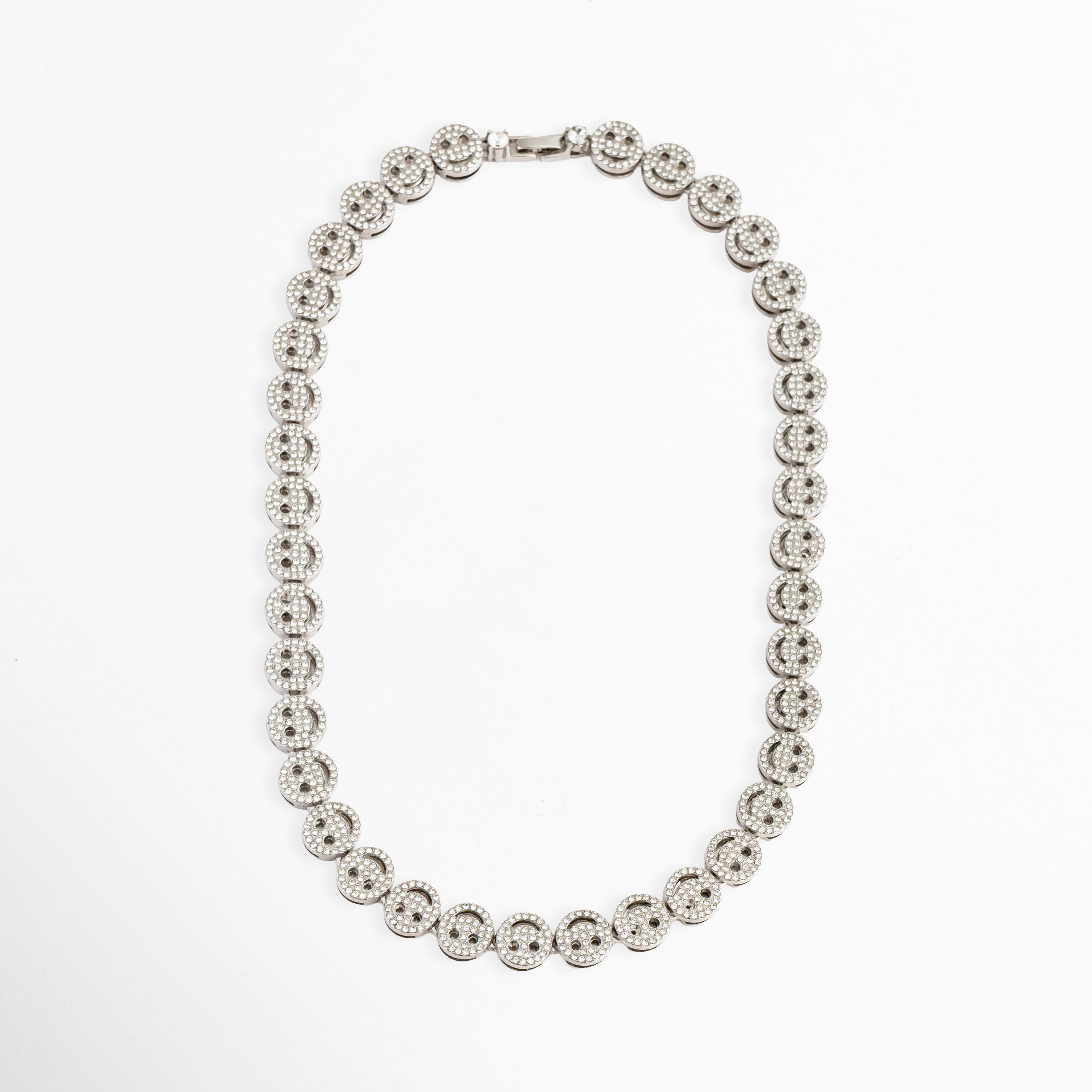 Vista completa del collar Felissia extendido en forma ovalada, Cadena completa de caritas felices en oro blanco de 50 cm de longitud, Collar de cobre con chapa de oro blanco y patrón continuo de smileys, Perspectiva general de gargantilla brillante de caras sonrientes para catálogo de Shopify, Gargantilla plateada de eslabones decorados con zirconias de inicio a fin.