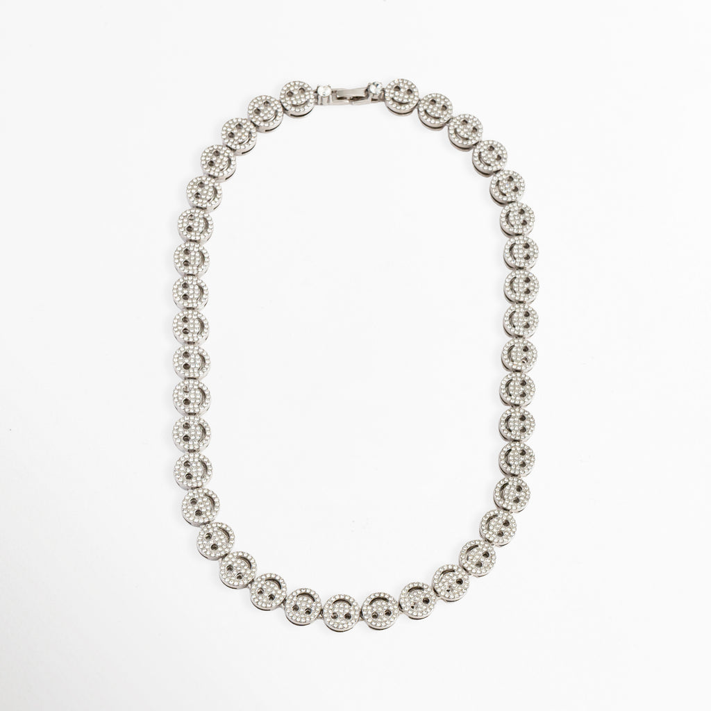 Vista completa del collar Felissia extendido en forma ovalada, Cadena completa de caritas felices en oro blanco de 50 cm de longitud, Collar de cobre con chapa de oro blanco y patrón continuo de smileys, Perspectiva general de gargantilla brillante de caras sonrientes para catálogo de Shopify, Gargantilla plateada de eslabones decorados con zirconias de inicio a fin.