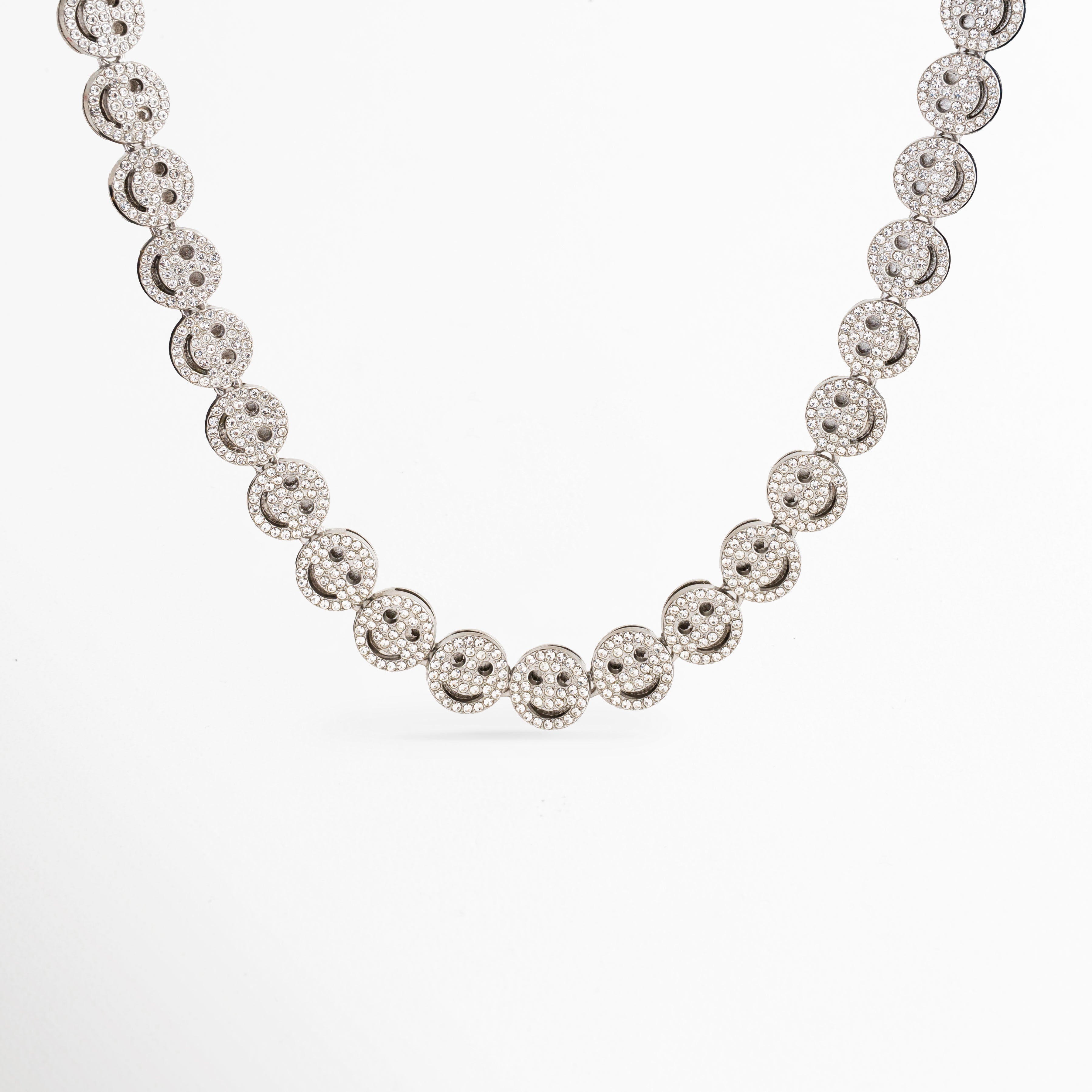 Collar Felissia plateado con eslabones en forma de caritas felices y zirconias, Gargantilla de oro blanco con diseño de caras sonrientes brillantes sobre fondo blanco, Collar de eslabones tipo smiley face chapado en oro blanco con piedras zirconias, Primer plano de cadena con dijes continuos de caritas felices de joyería fina, Detalle frontal del collar Felissia resaltando el brillo de las zirconias incrustadas.