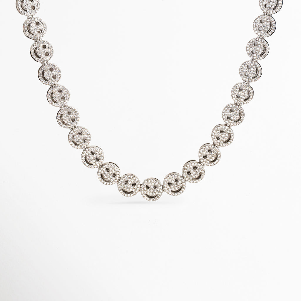 Collar Felissia plateado con eslabones en forma de caritas felices y zirconias, Gargantilla de oro blanco con diseño de caras sonrientes brillantes sobre fondo blanco, Collar de eslabones tipo smiley face chapado en oro blanco con piedras zirconias, Primer plano de cadena con dijes continuos de caritas felices de joyería fina, Detalle frontal del collar Felissia resaltando el brillo de las zirconias incrustadas.